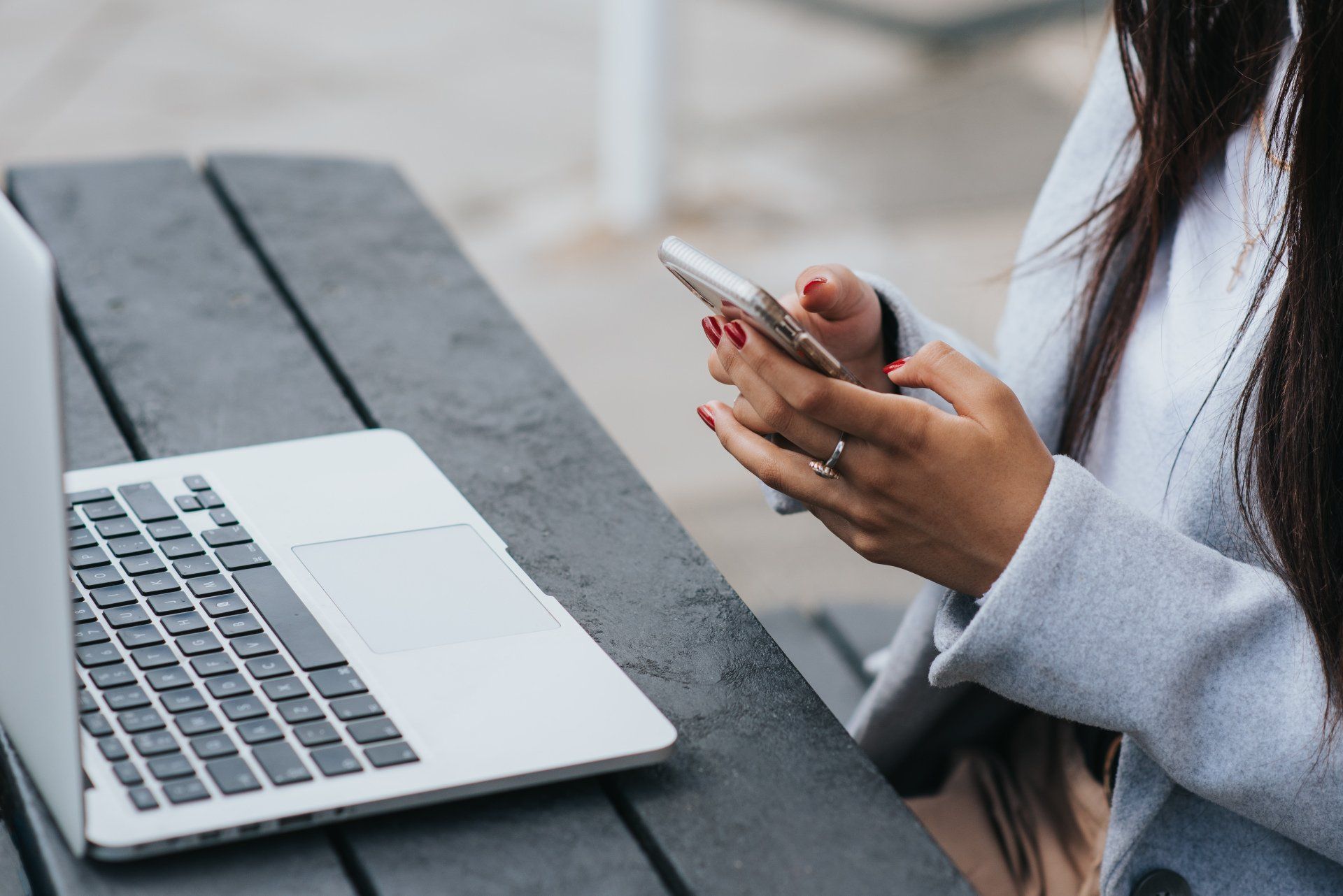 A woman is sitting at a table using a laptop and a cell phone.