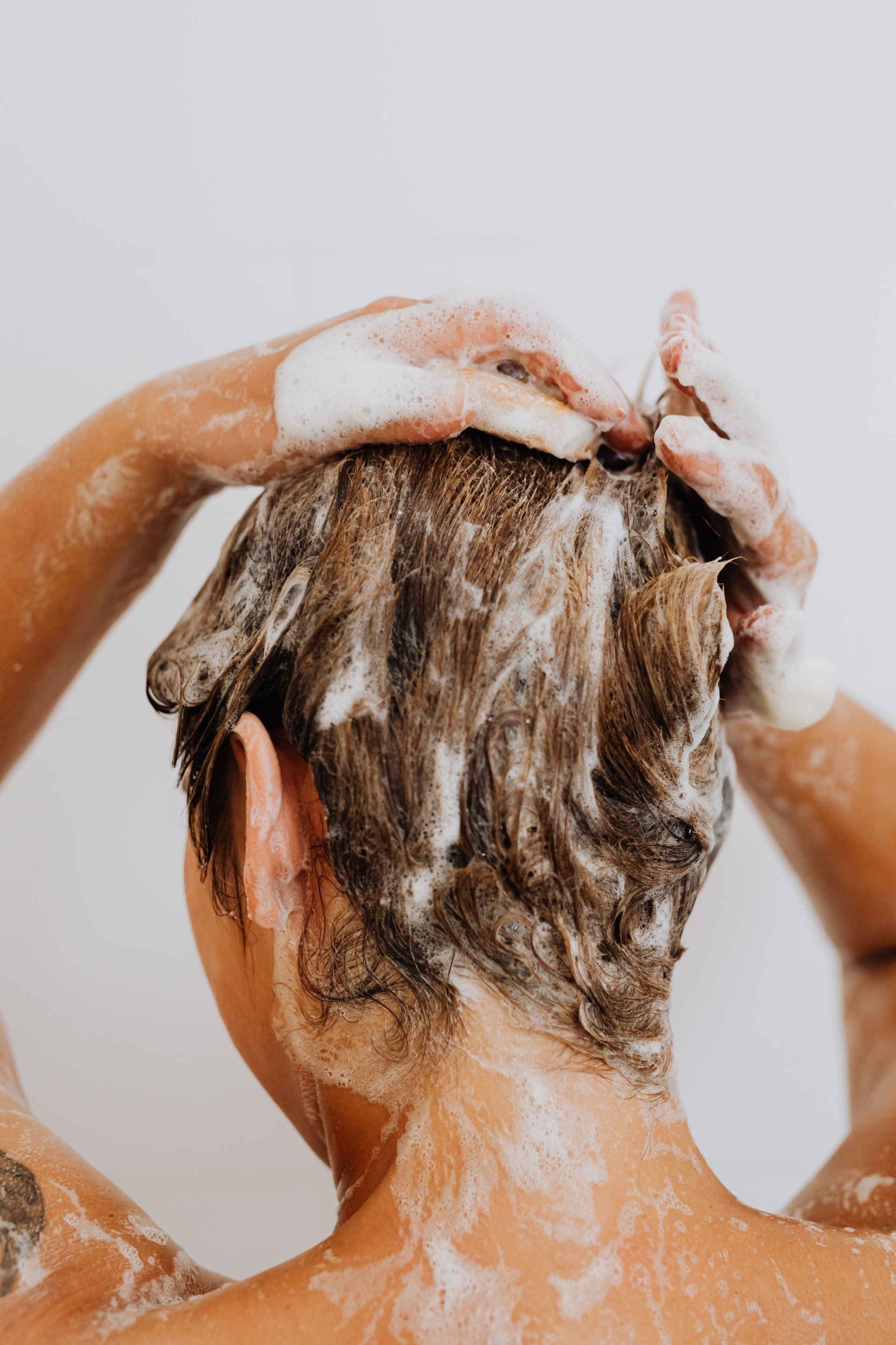 A woman is washing her hair in the shower with soap.