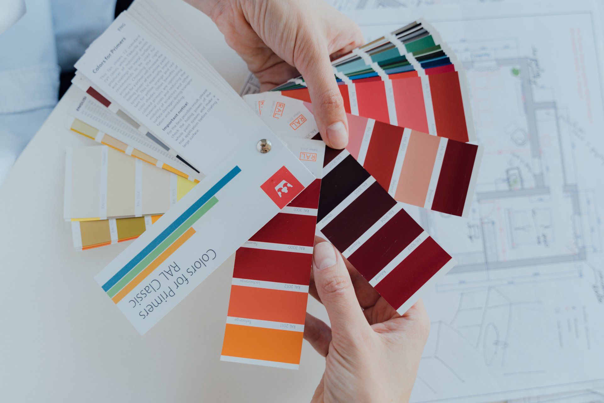 Hands holding color swatches for design choices, with a blueprint in the background.