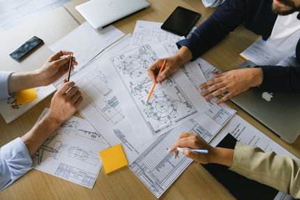 A group of people are sitting around a table looking at blueprints.