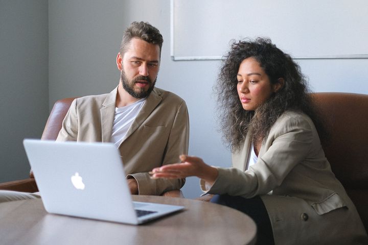 Two people discussing beside an open laptop on a couch in a living room