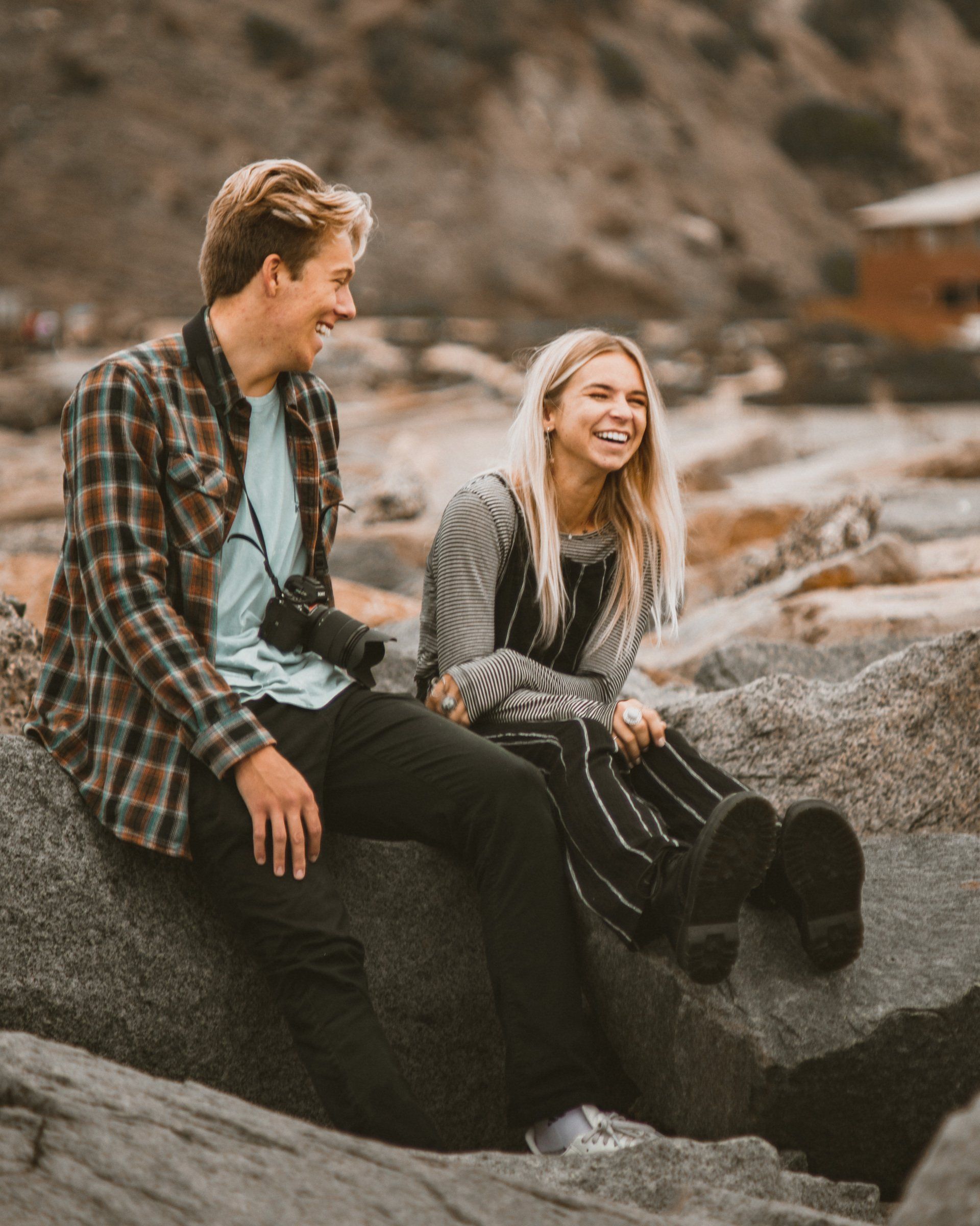 A man and a woman are sitting on a rock and laughing.
