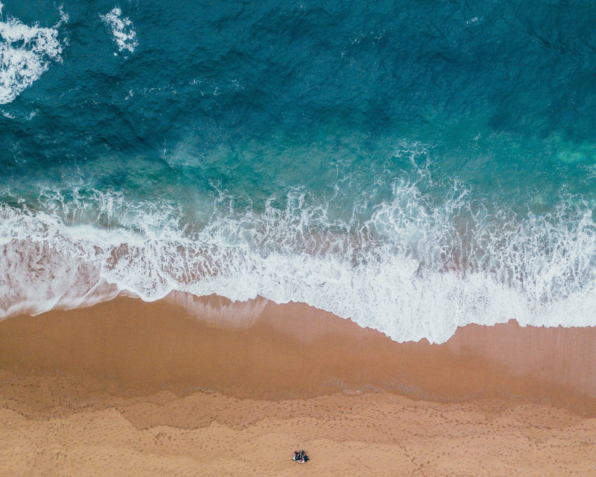 An aerial view of a beach with waves crashing on the sand.