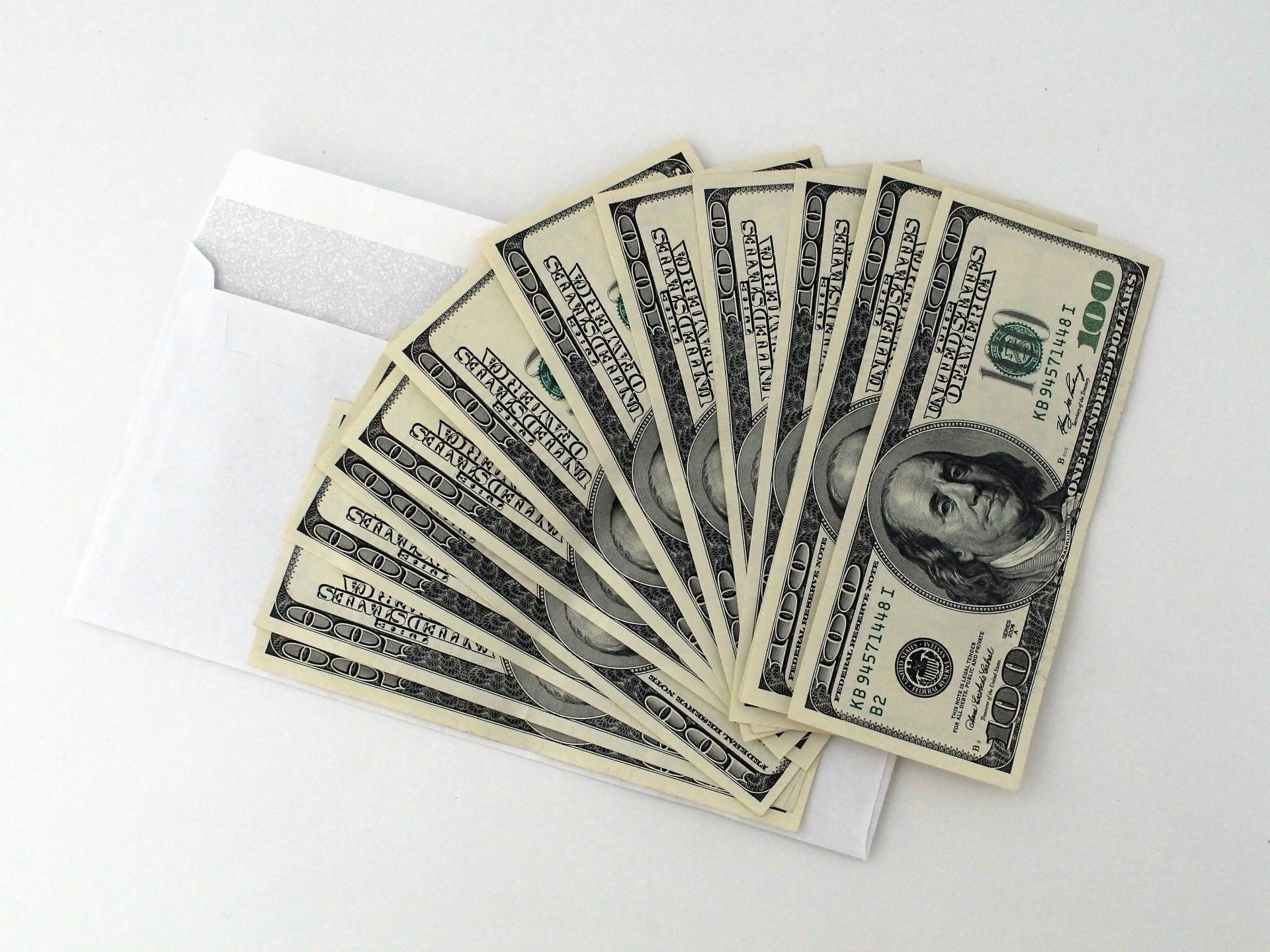 Fan of hundred-dollar bills emerging from a white envelope.