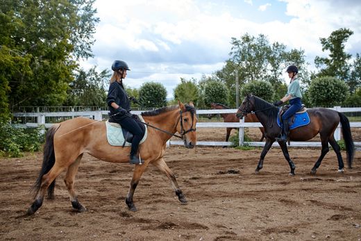 Two people are riding horses in a dirt field.