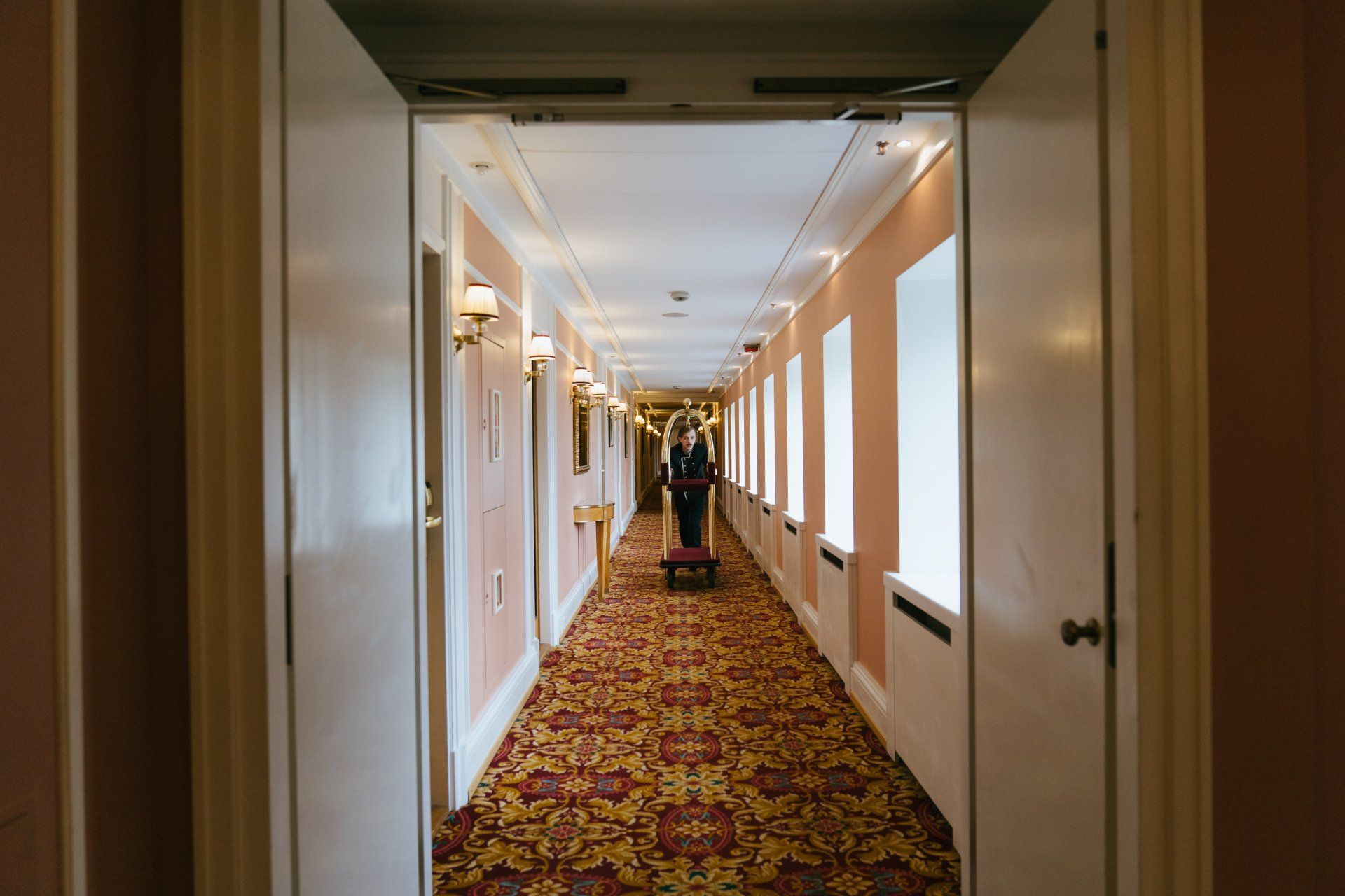 A long hallway in a hotel with a red carpet and white walls.