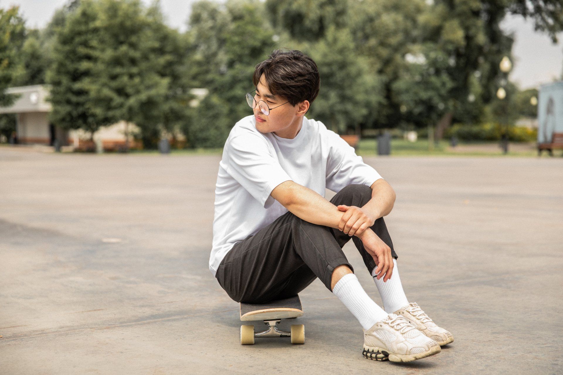 Een persoon met een bril zit op een skateboard in een park en kijkt over zijn schouder.
