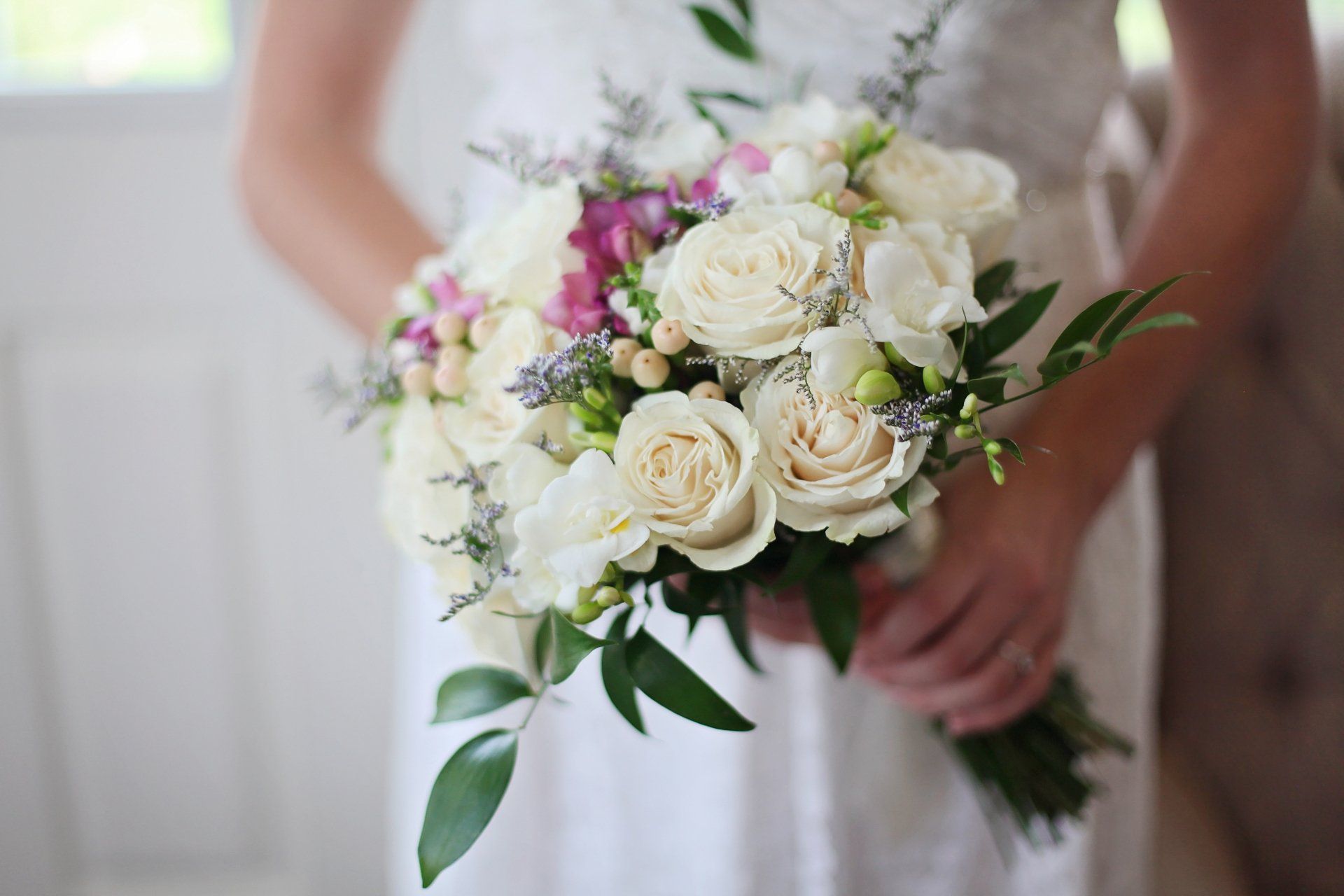 A bride in a white dress is holding a bouquet of white and pink flowers.