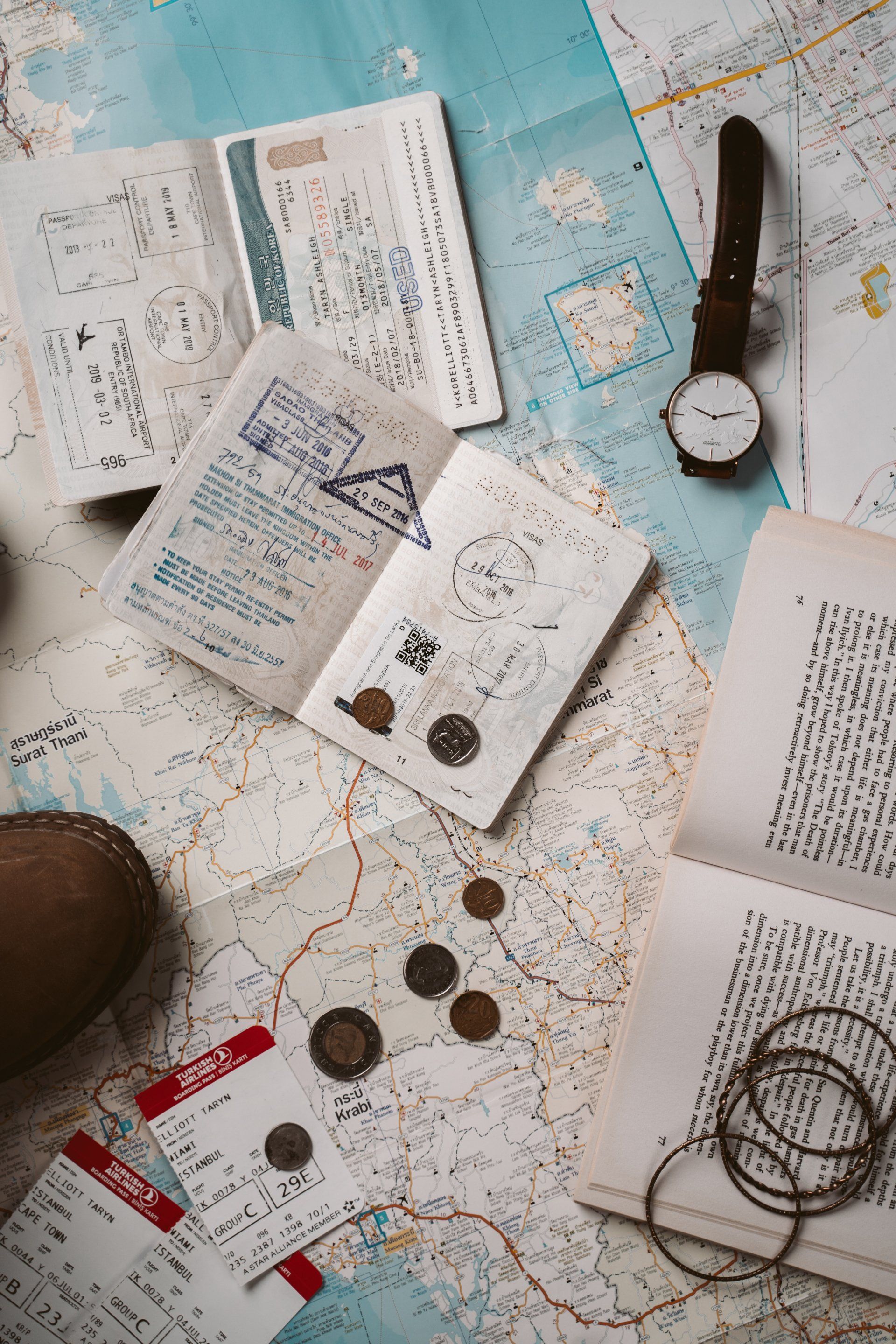 A map , passports , coins , a watch , and a book are on a table.
