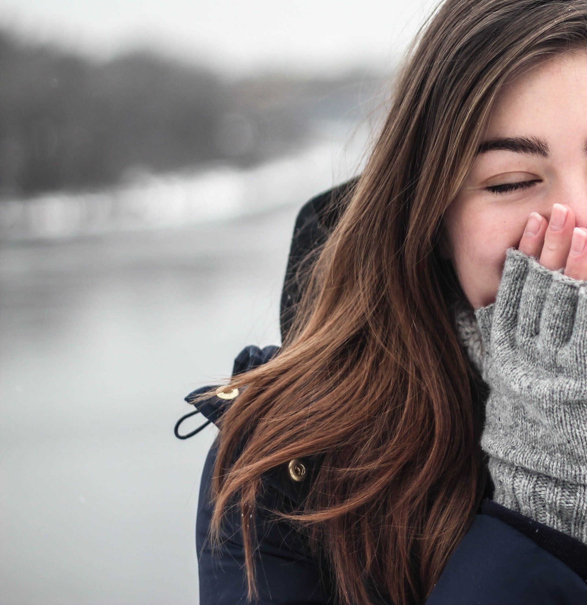 A woman wearing a sweater and gloves is covering her mouth with her hand.