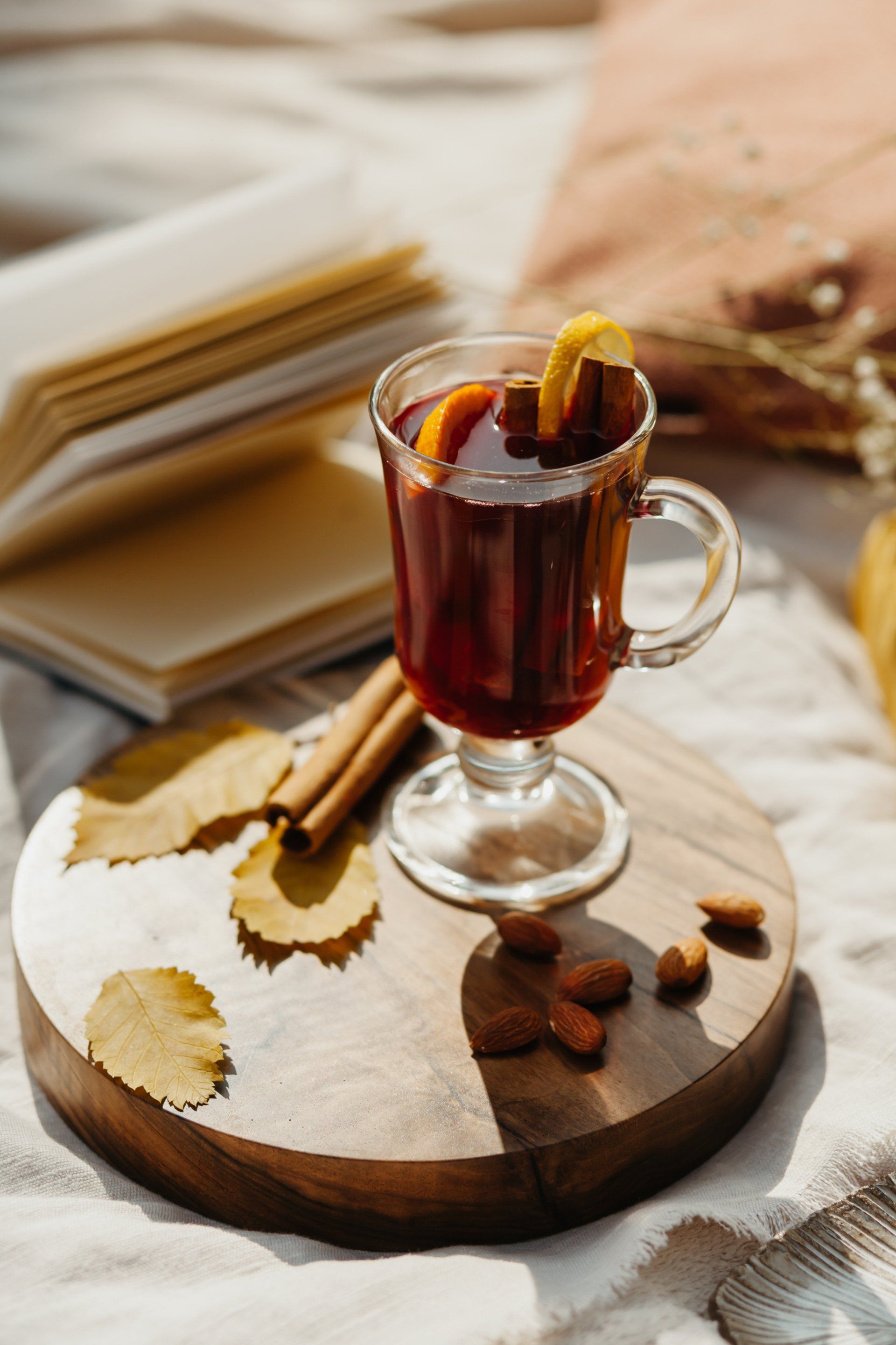 Un verre de vin chaud avec des bâtons de cannelle et des amandes sur une planche à découper en bois.