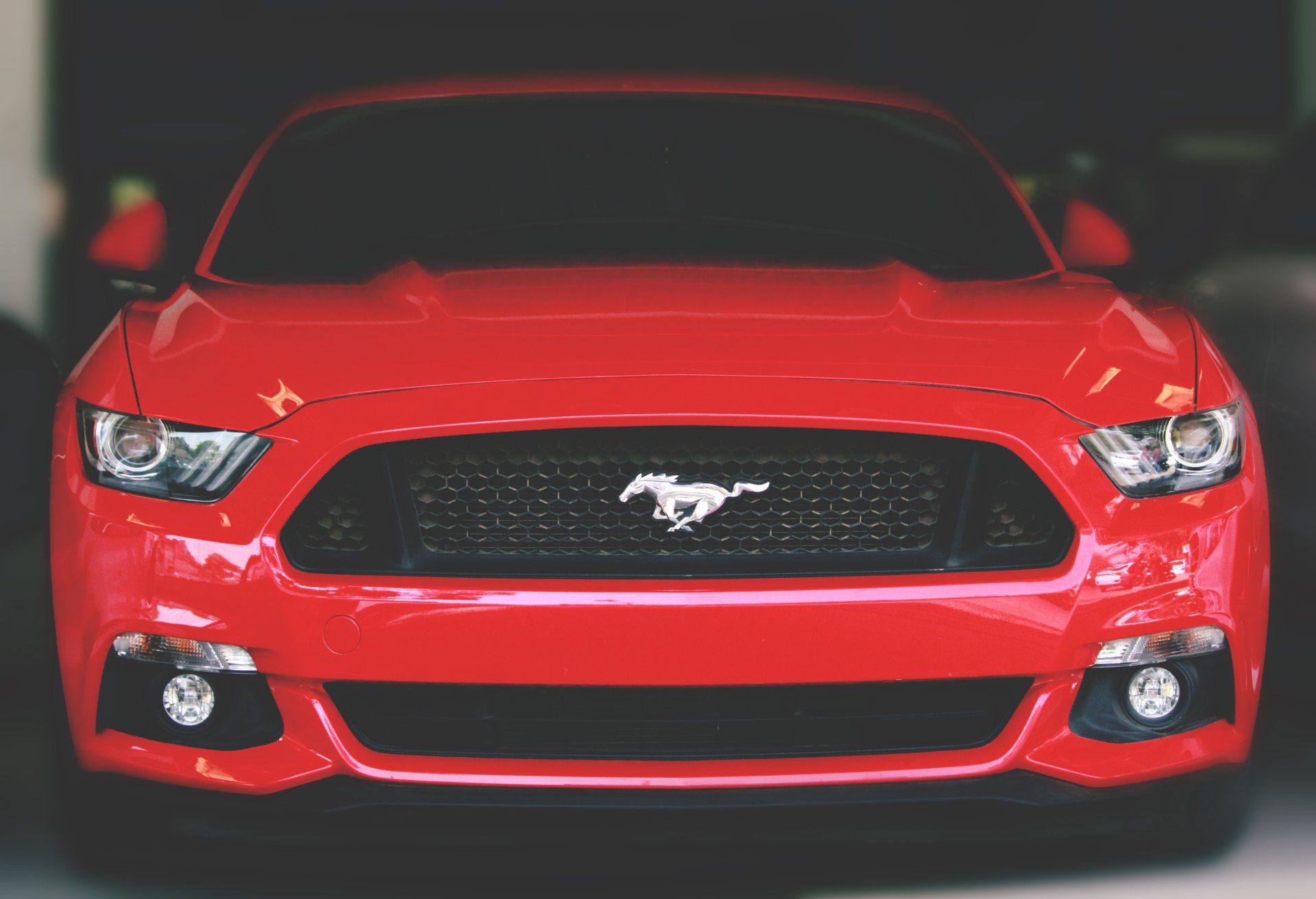 Red Ford Mustang, front view, black grill with horse emblem, headlights.
