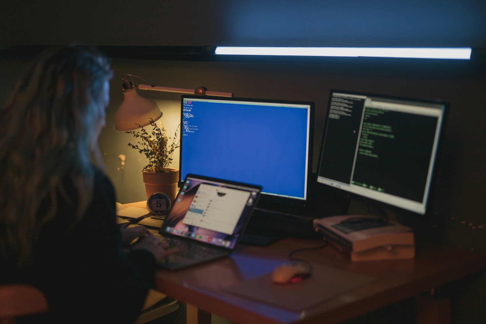 Reboot Tech working at a desk with three monitors. One shows code, the other a blue screen