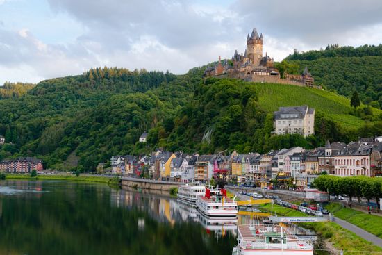 castle sitting on hills A castle is sitting on top of a hill next to a river.