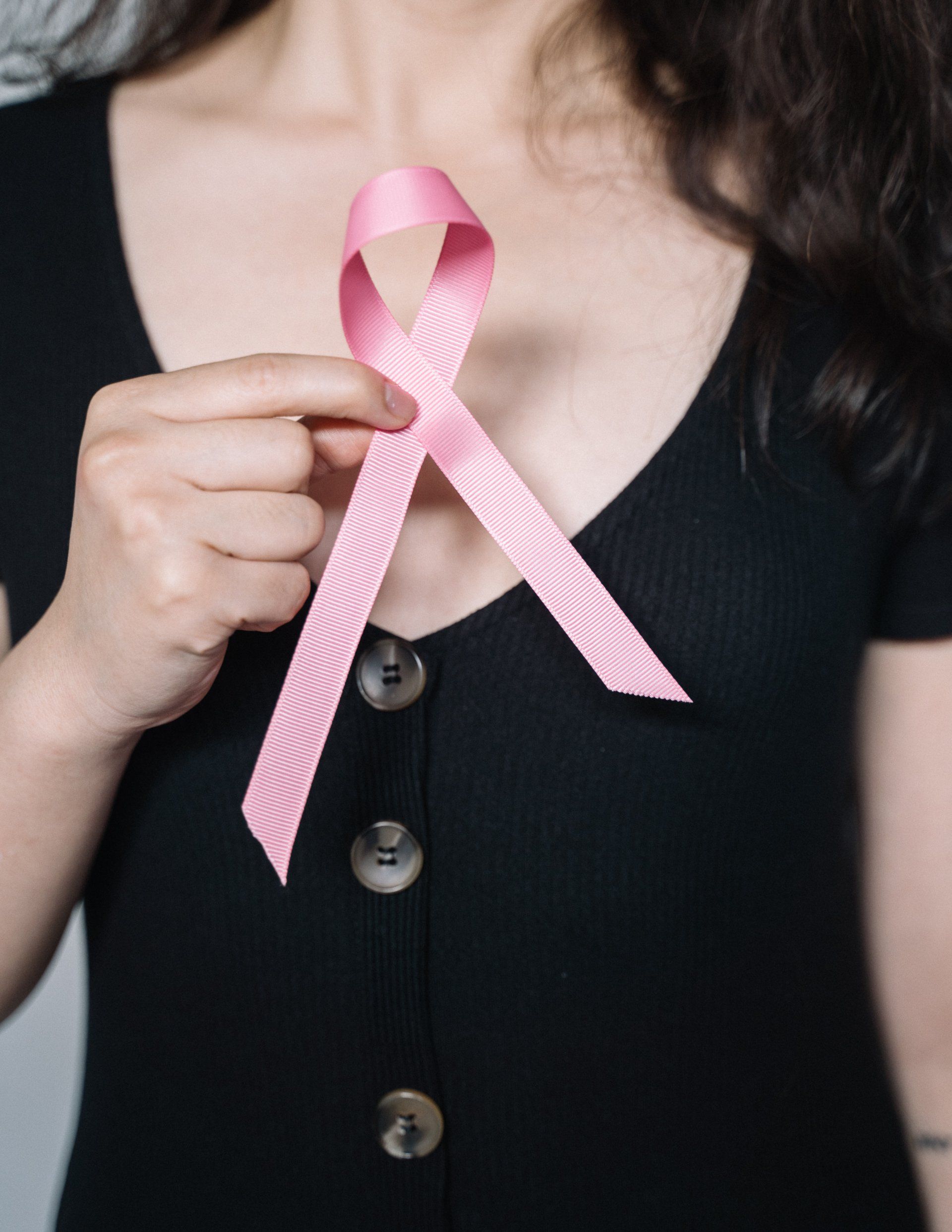 Woman wearing a black top, holding a pink ribbon, a symbol of breast cancer awareness.