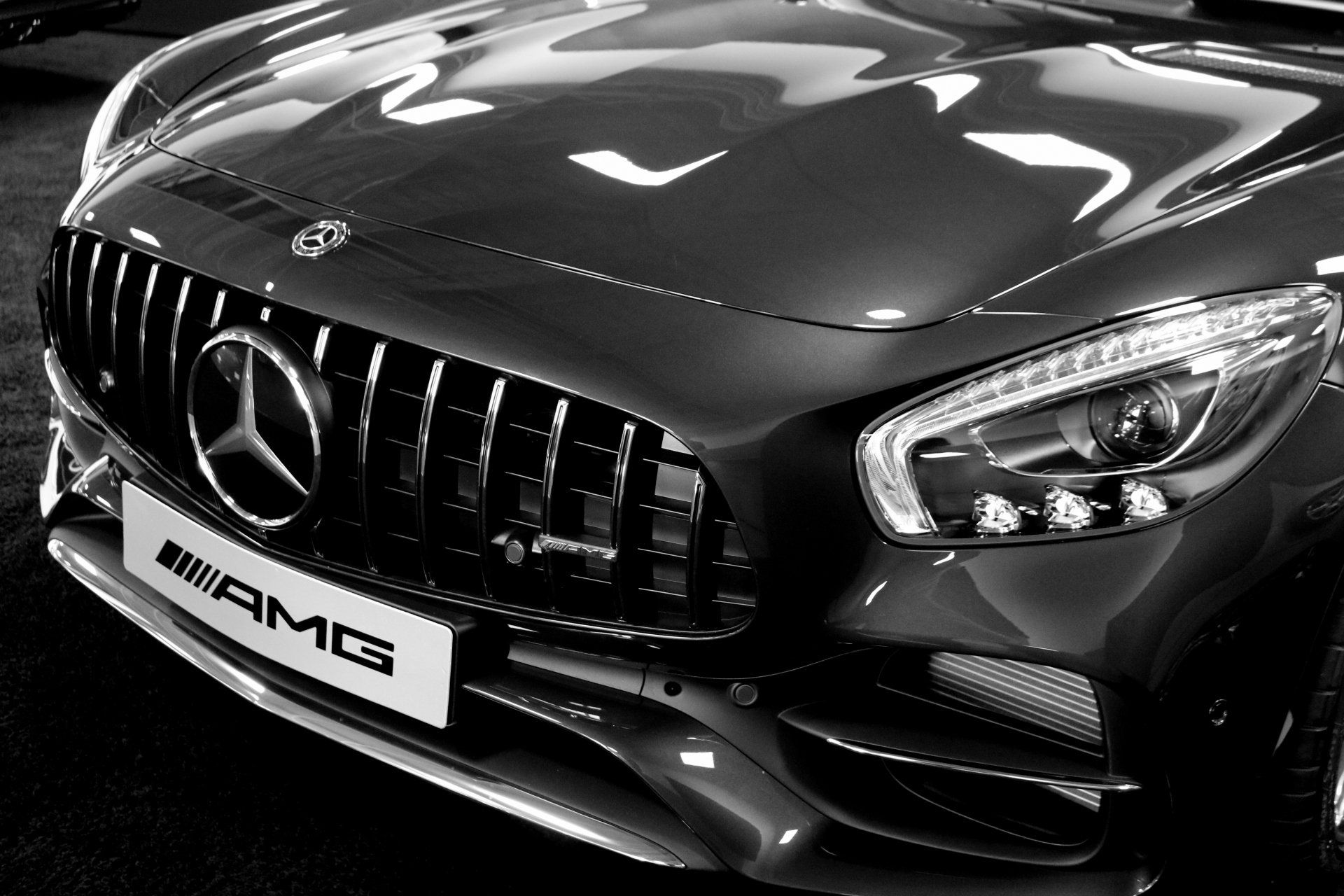 Black and white close-up of a Mercedes-AMG sports car with a prominent front grill and logo.