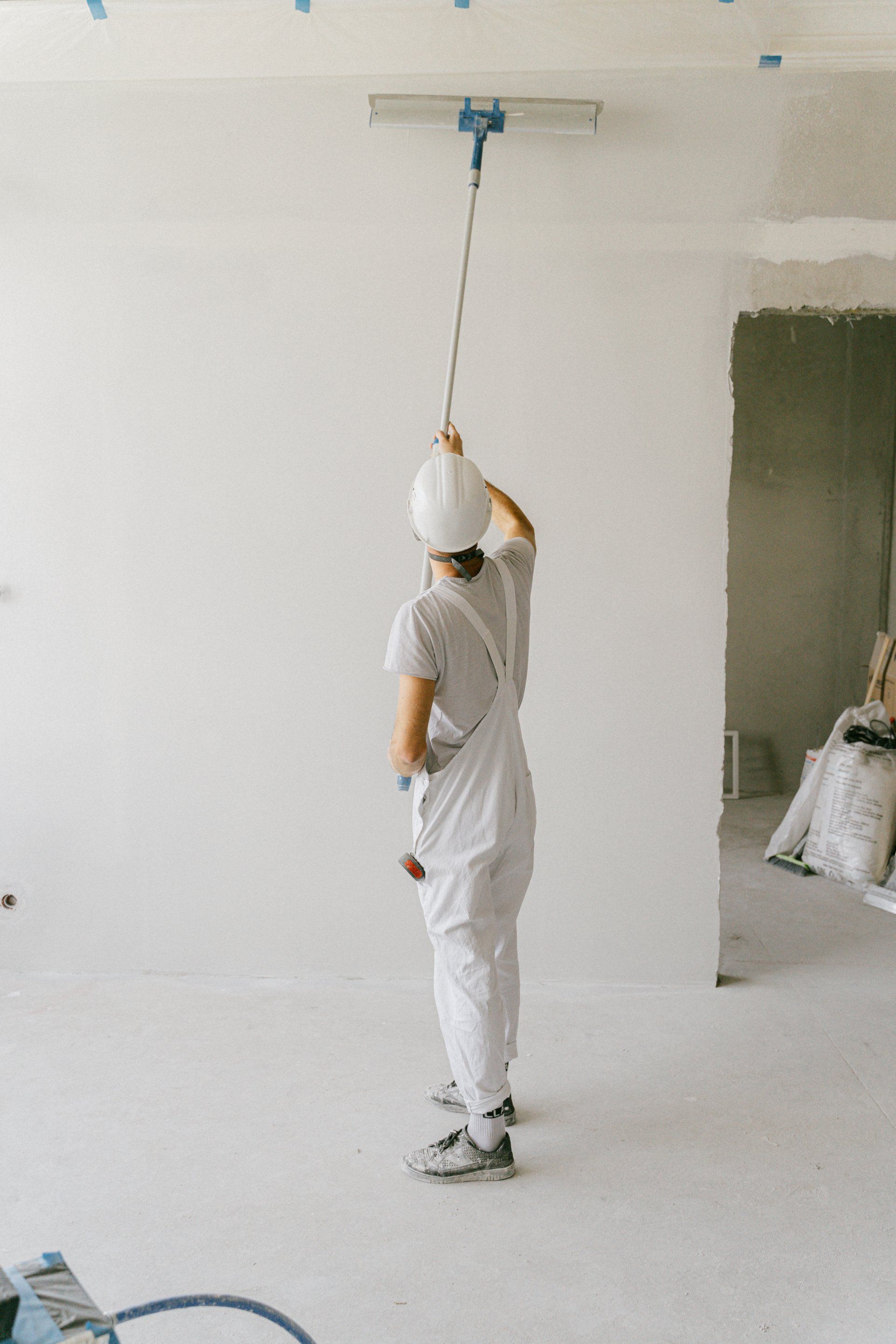 Worker in white paint suit using a ceiling pole in a room under renovation