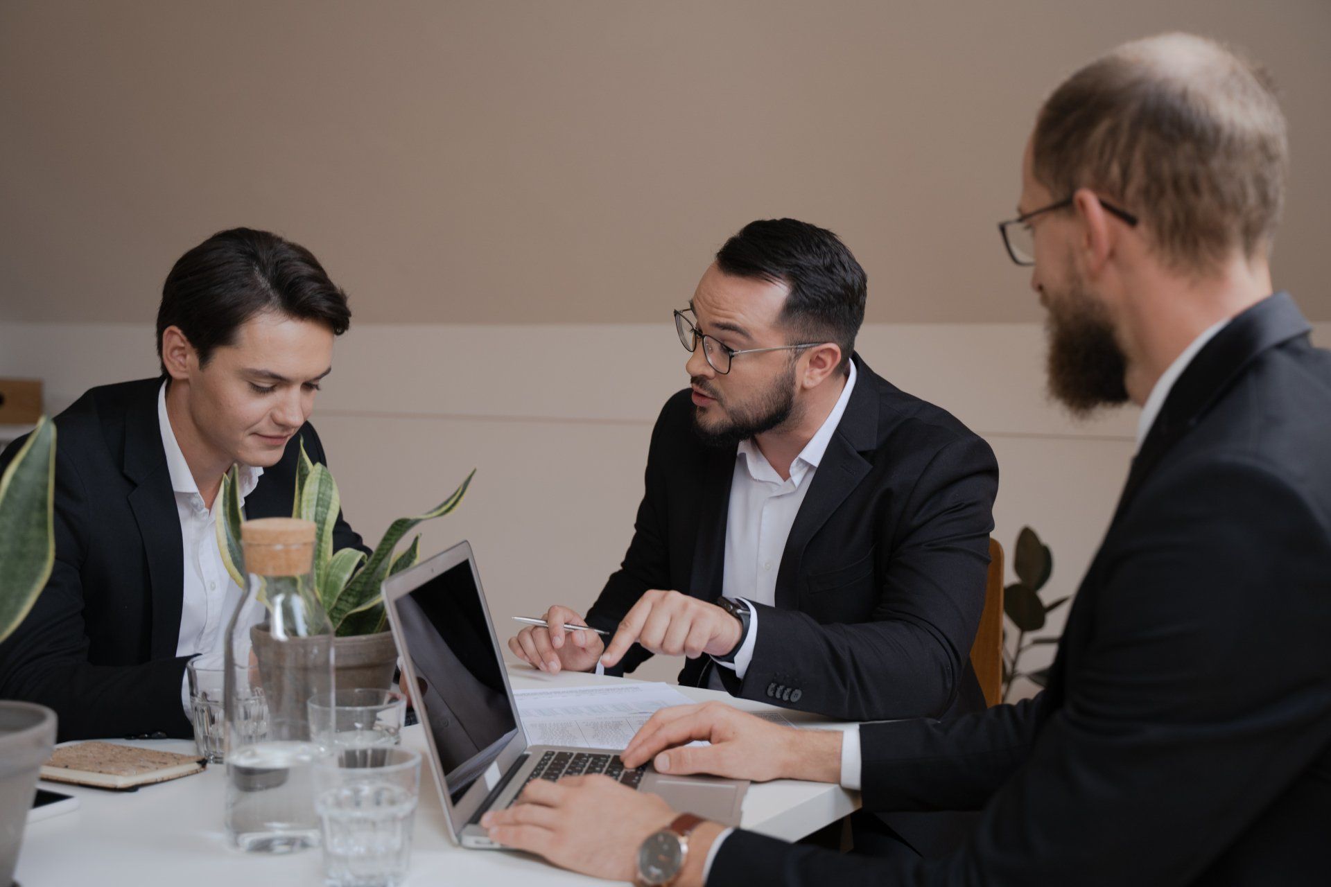 A group of men are sitting around a table with laptops.