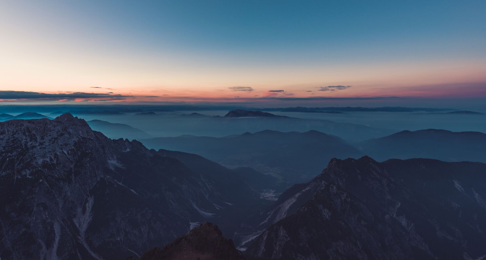 An aerial view of a mountain range at sunset with clouds in the background.