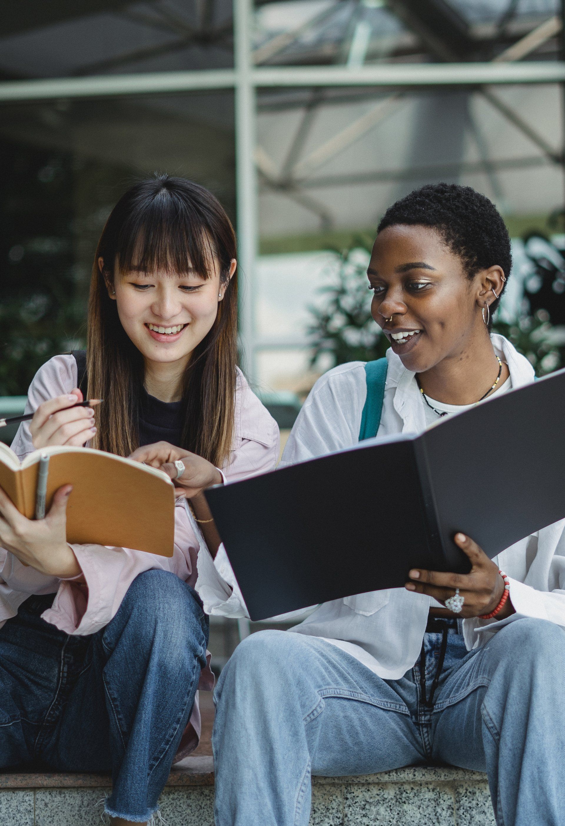 Two young women are sitting on steps reading books.
