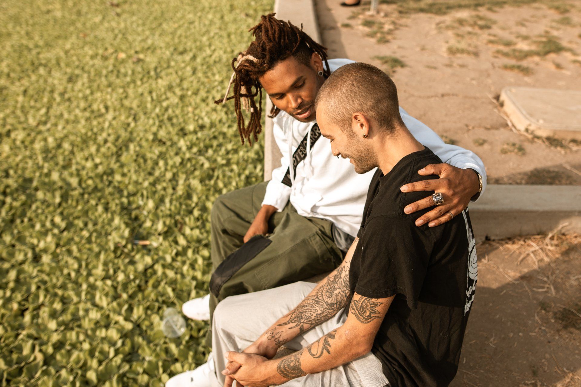 Two men are sitting next to each other on a sidewalk.