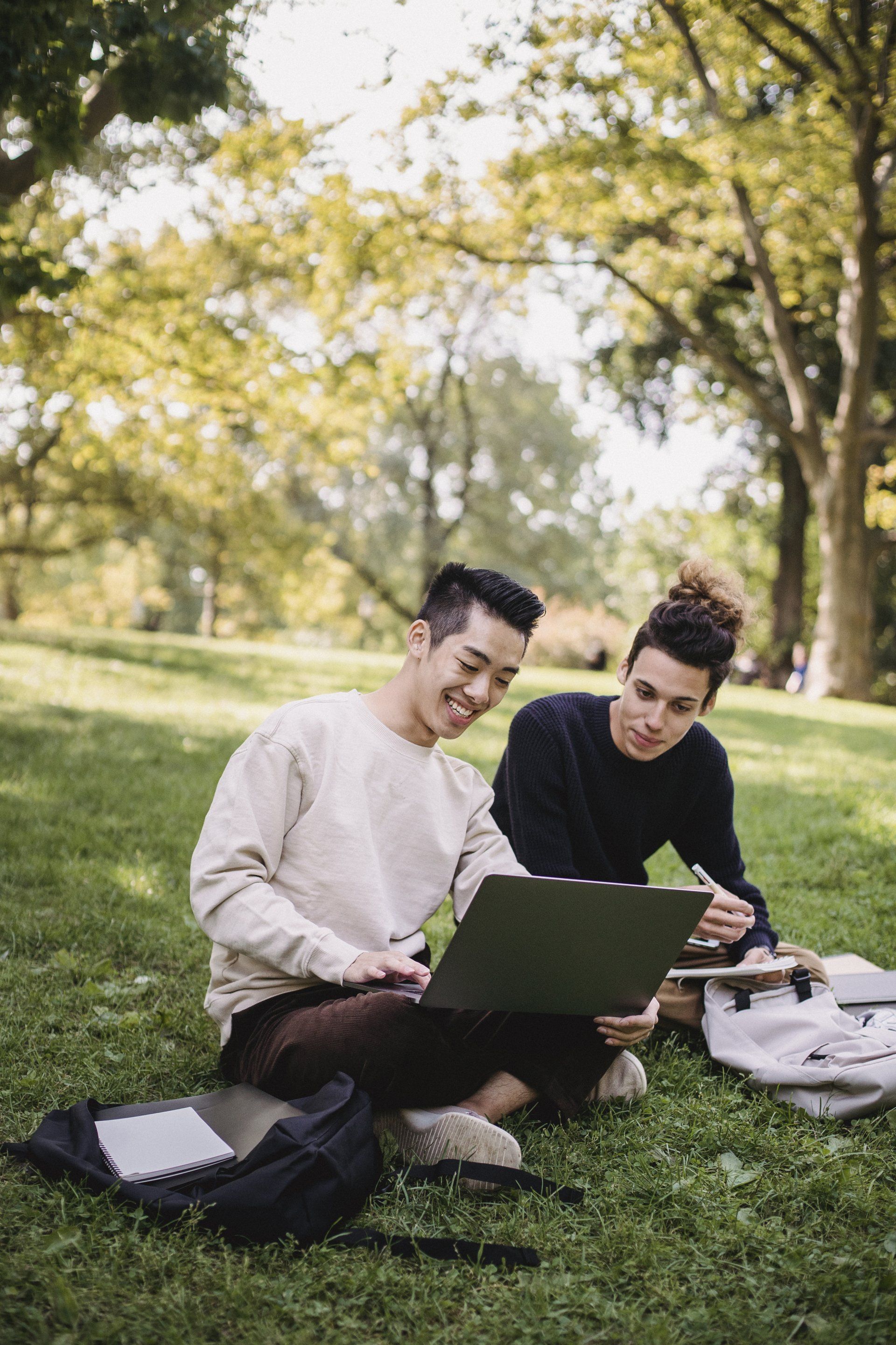 two men sit on the grass looking at a laptop