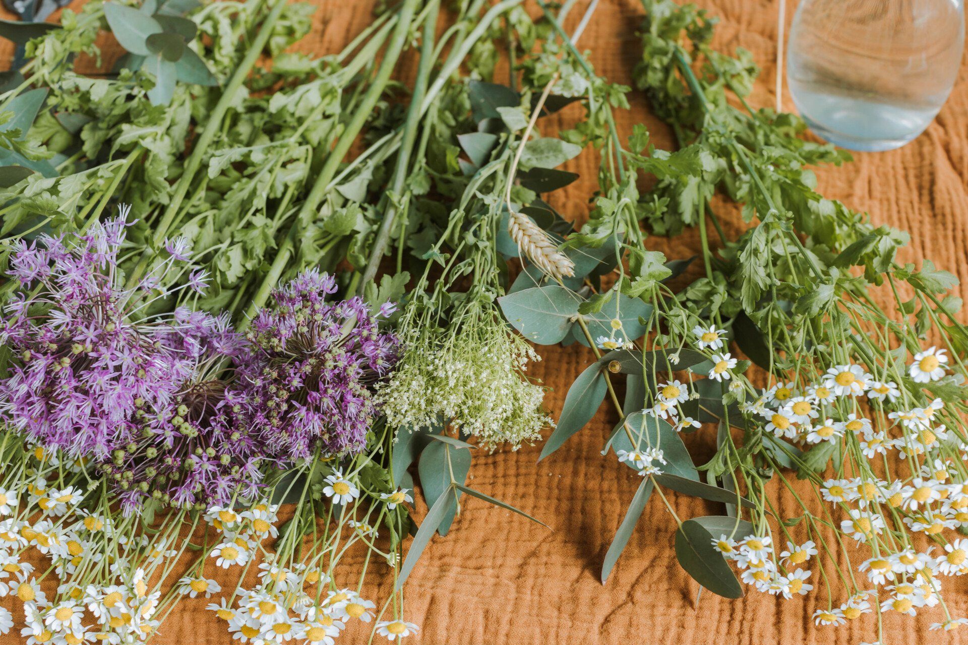 Verschiedene Wildblumen und Grünpflanzen auf einem Holztisch, oben rechts ein Glasgefäß.