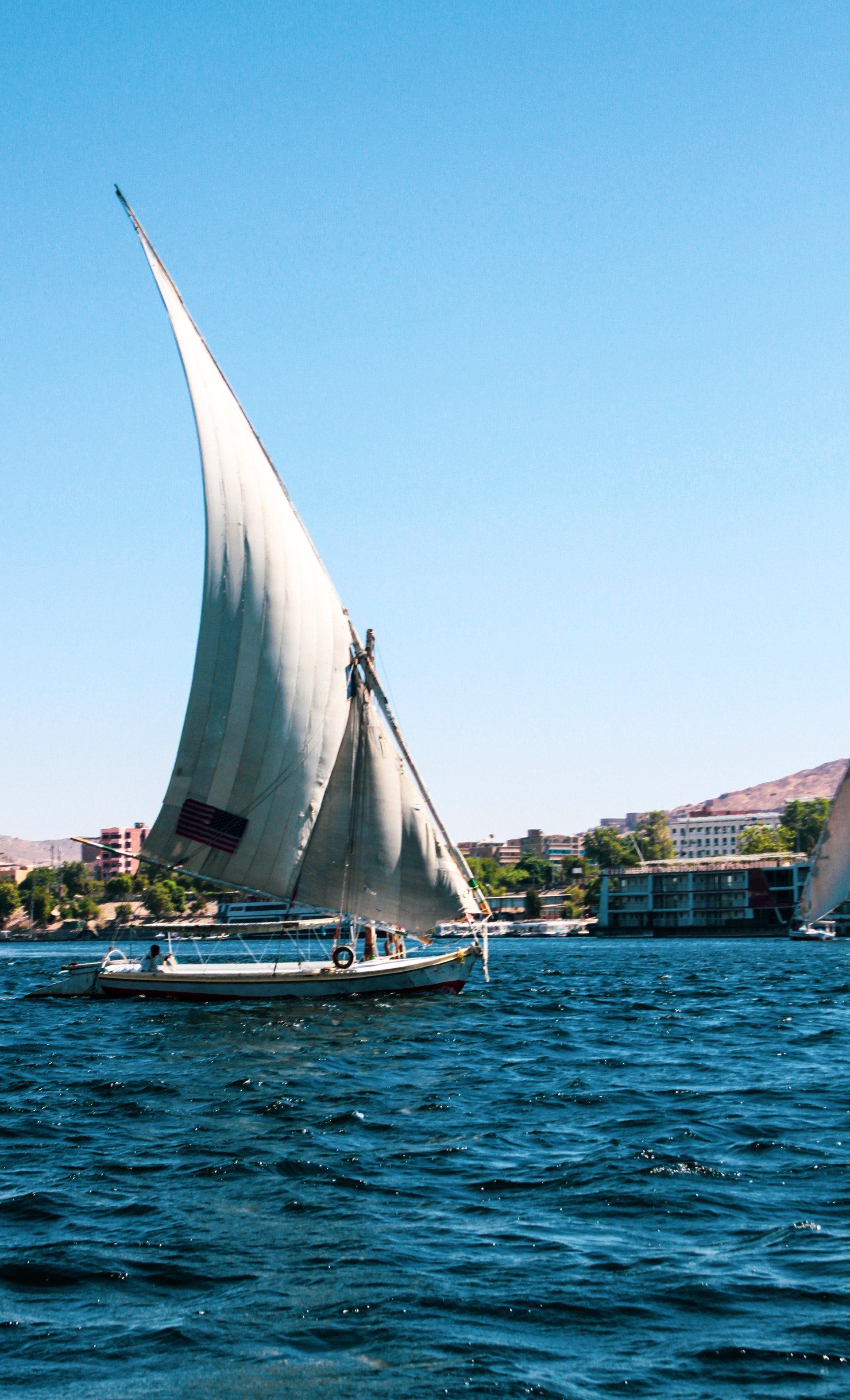 Sailboat with white sail on blue water, under a bright blue sky.