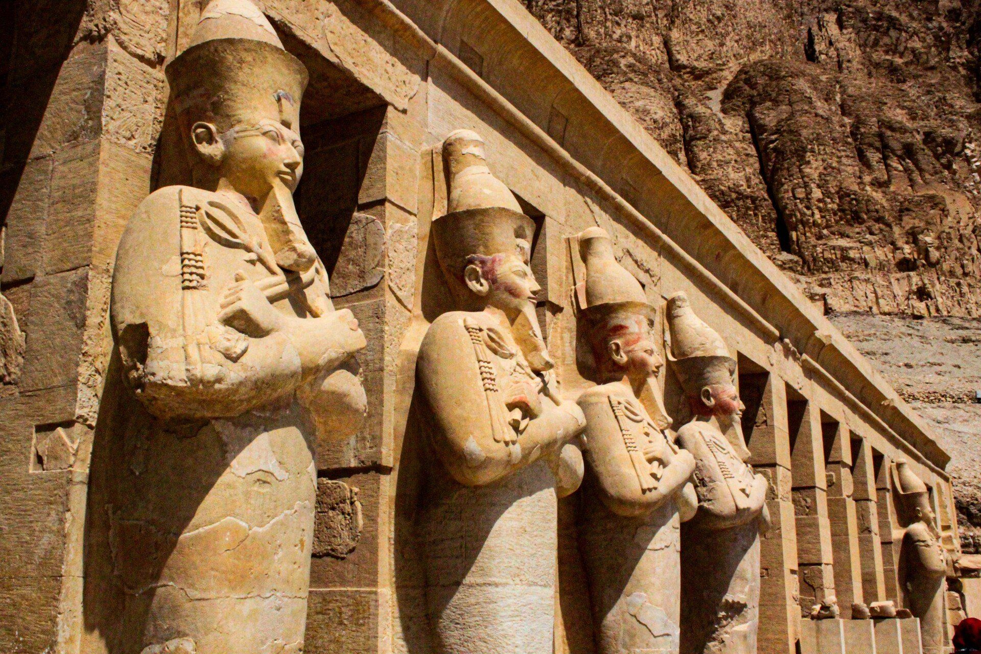 Statues of pharaohs with headdresses line a wall in an ancient temple, likely in Egypt.