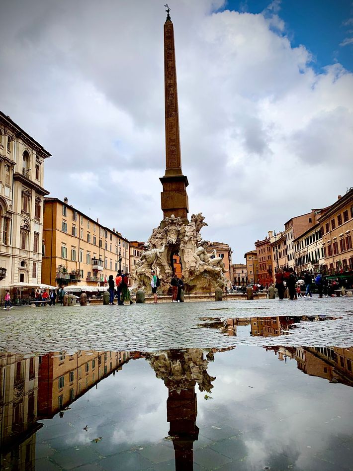 A large obelisk is reflected in a puddle of water