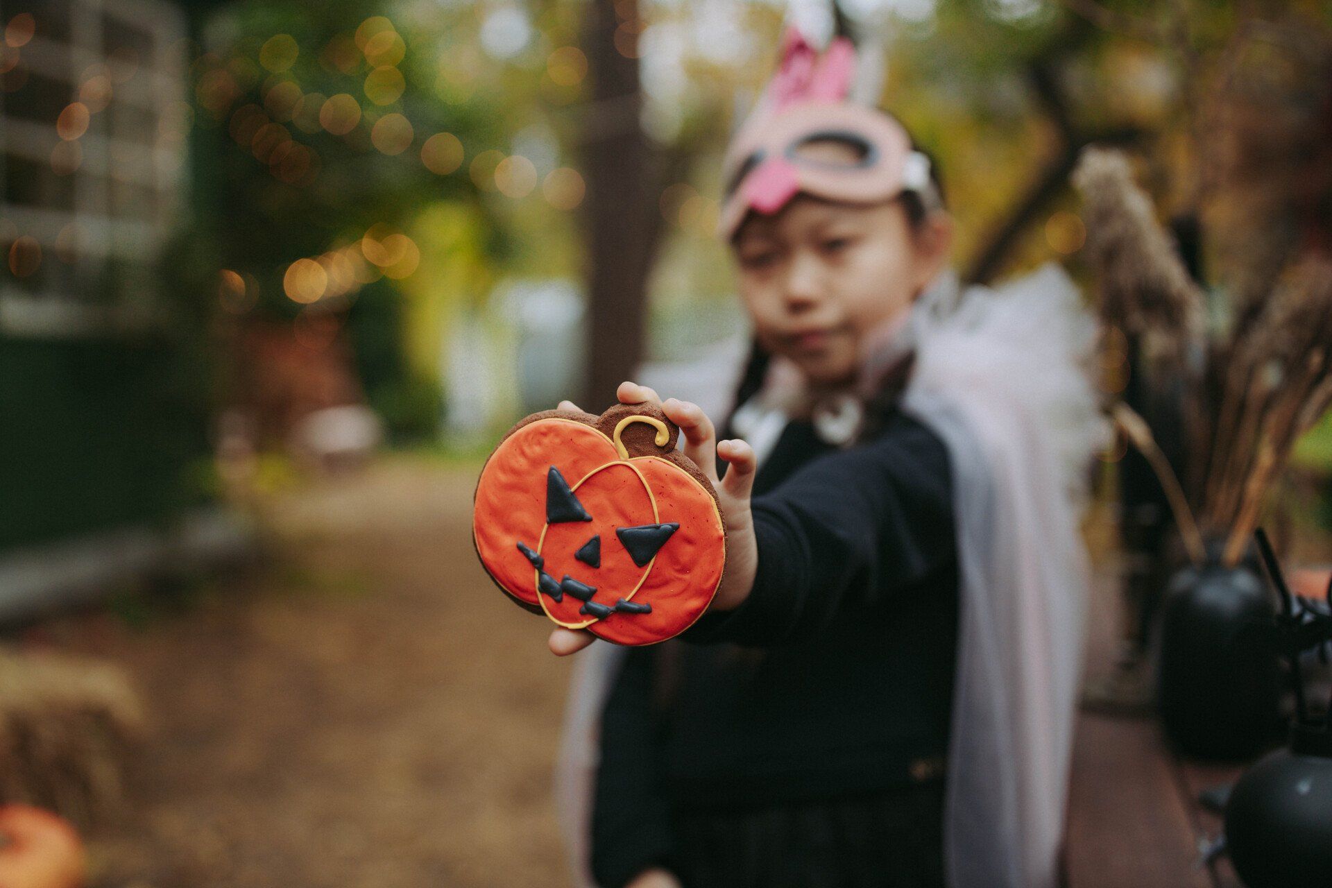 A little girl in a halloween costume is holding a pumpkin cookie.