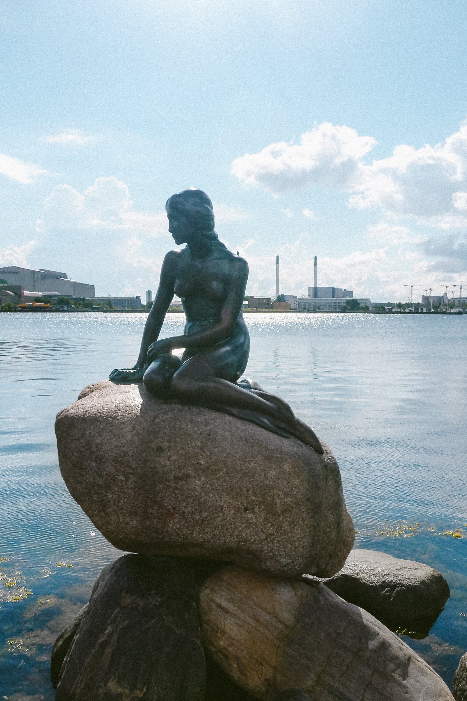 En statue av en havfrue sitter på en stein i vannet.