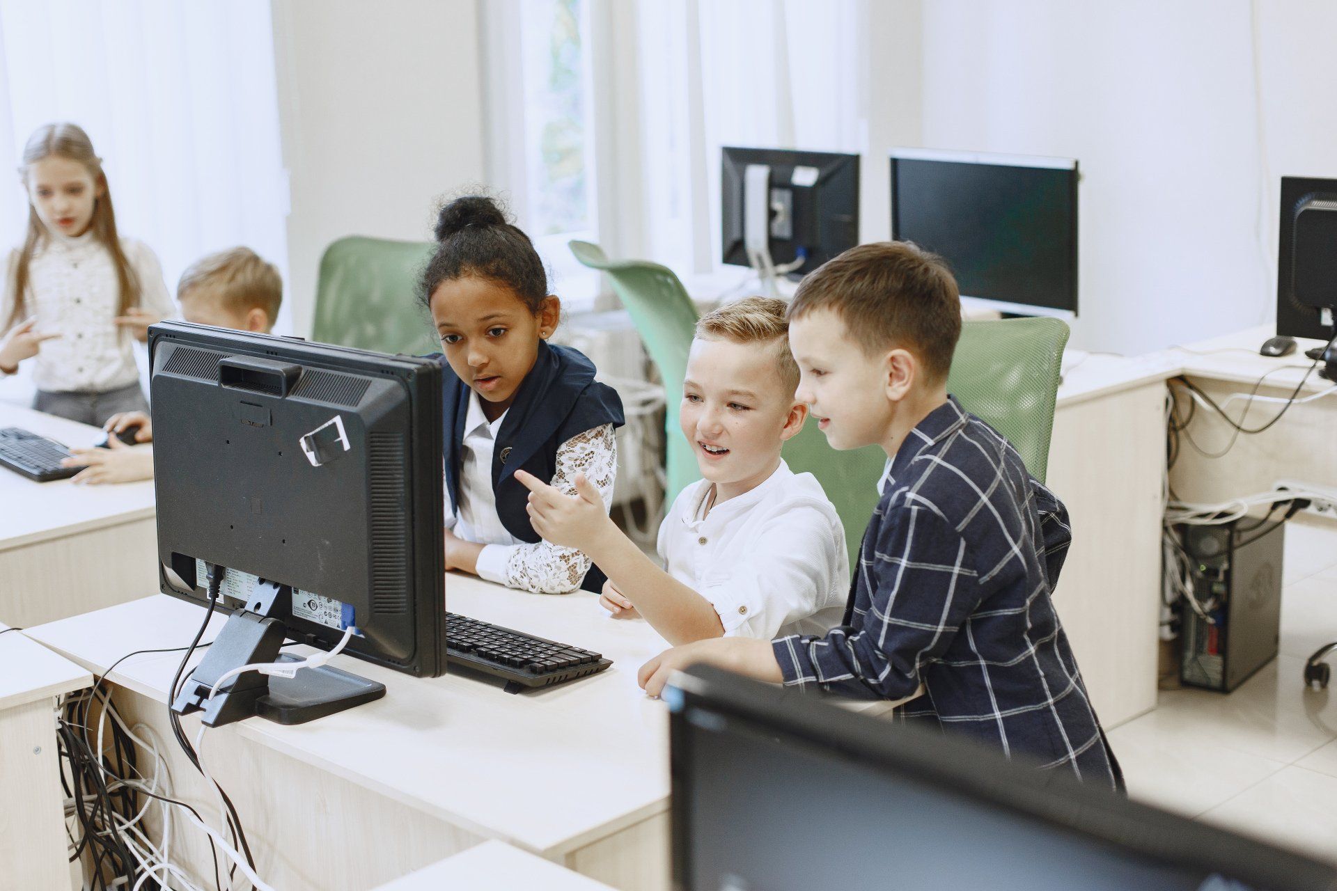 Children looking at a computer monitor in a classroom setting, one pointing.