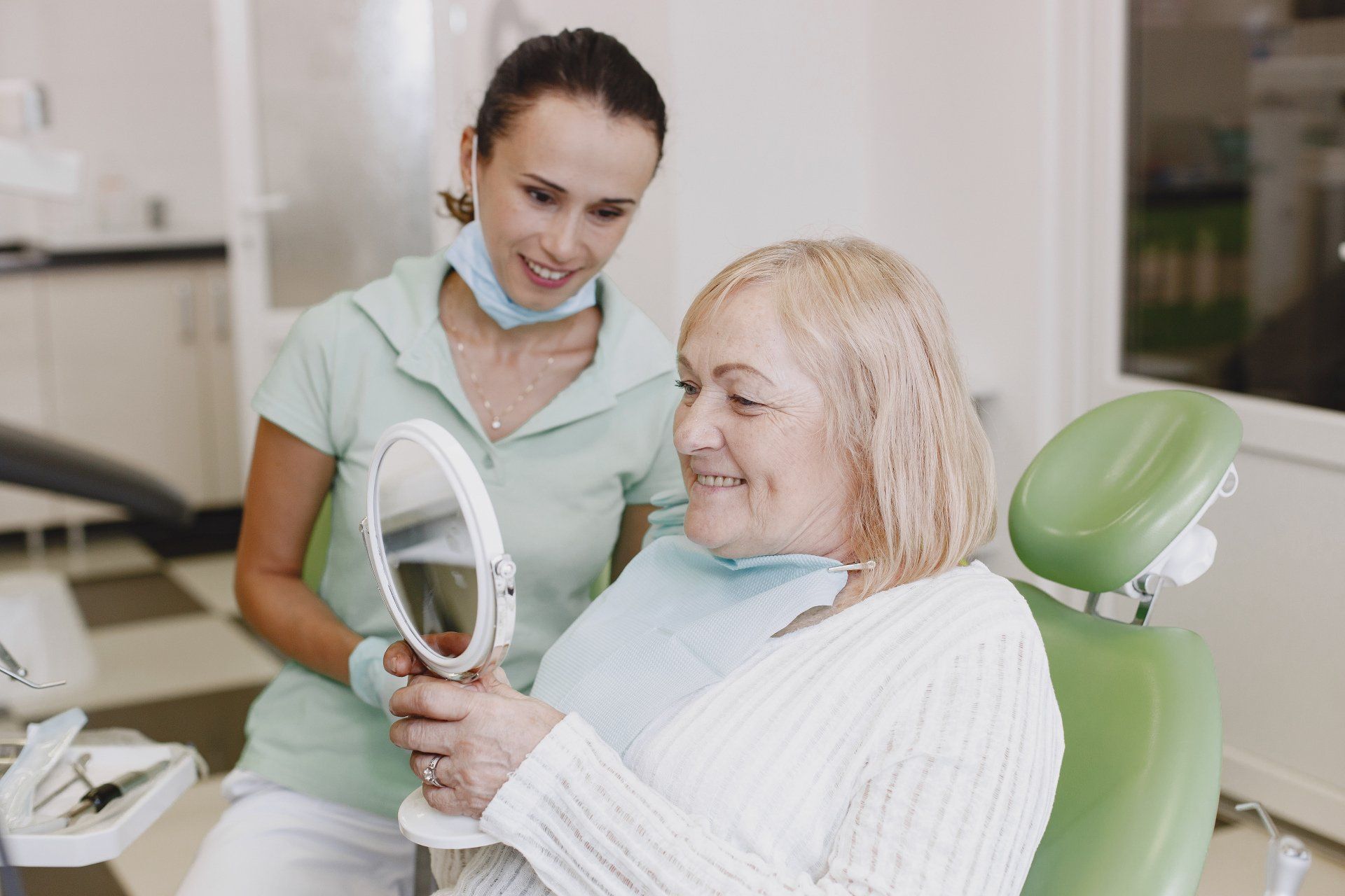 A woman is sitting in a dental chair looking at her teeth in a mirror after getting dentures in Lees Summit MO.