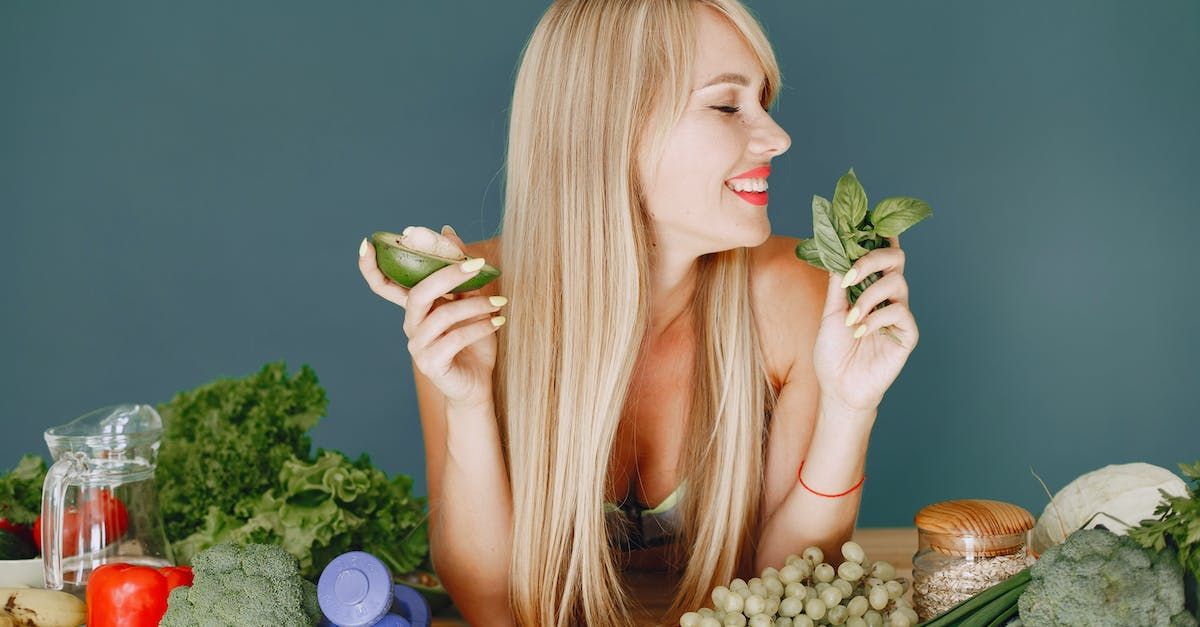 a woman holding an avocado and a sprig of basil