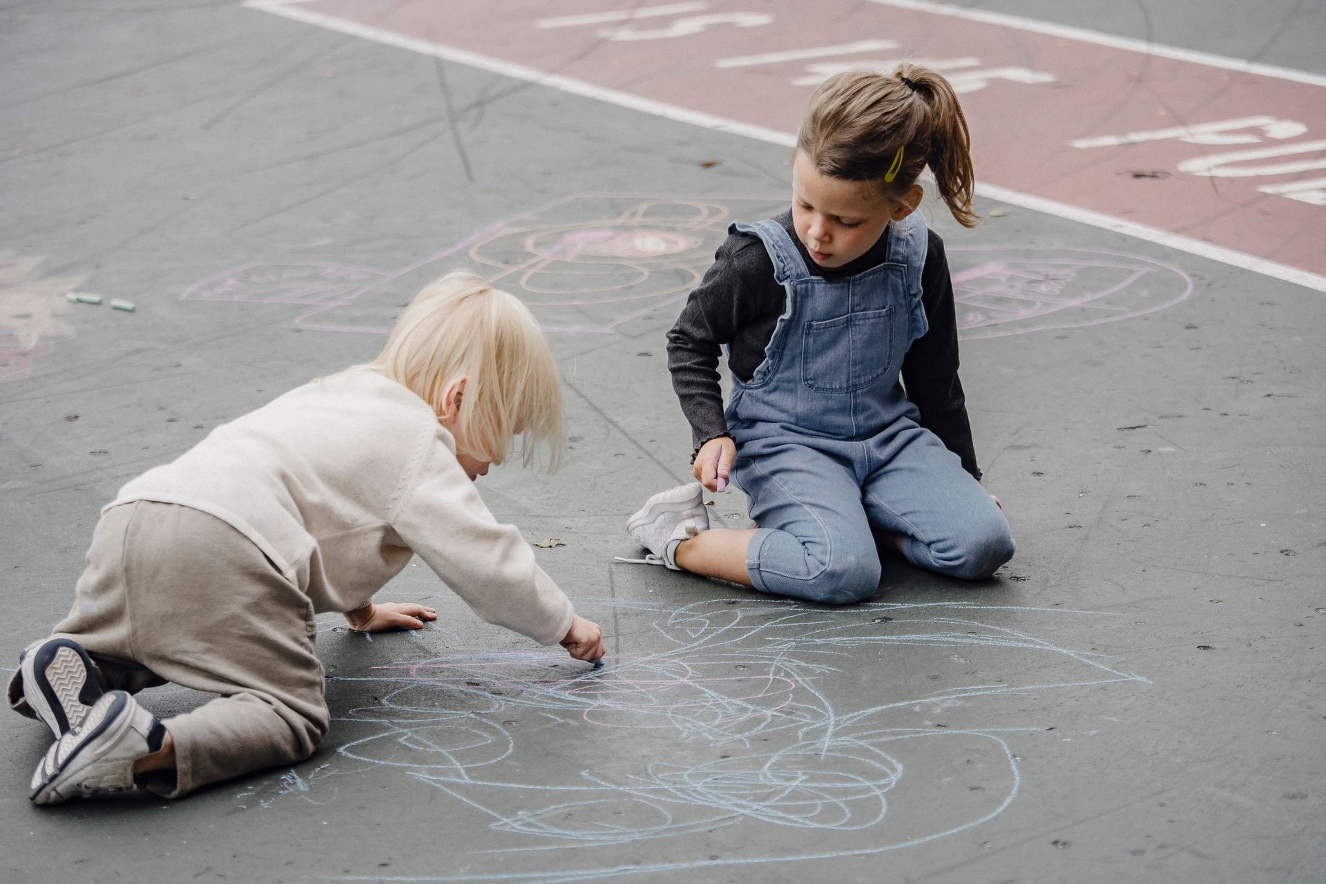 Two little girls are sitting on the ground drawing with chalk.