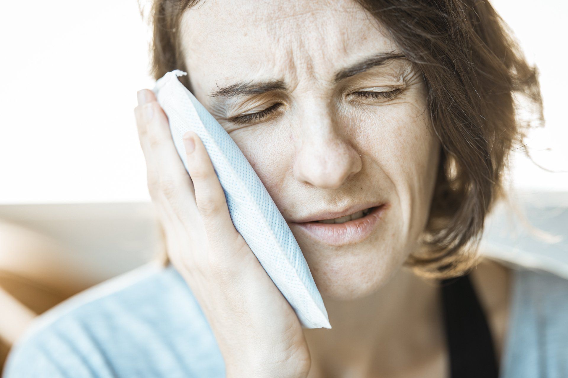 Woman Holding a Cold Compress to Cheek, Grimacing in Pain — The Denture Care Group Sunshine Coast in Caloundra, QLD