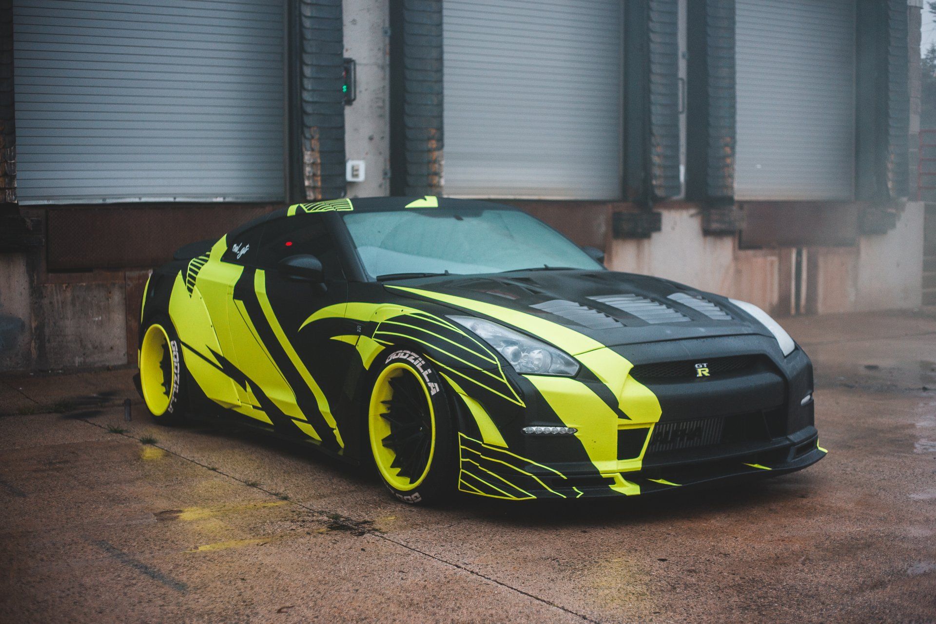 Black and neon yellow Nissan GT-R sports car parked in front of a loading dock.