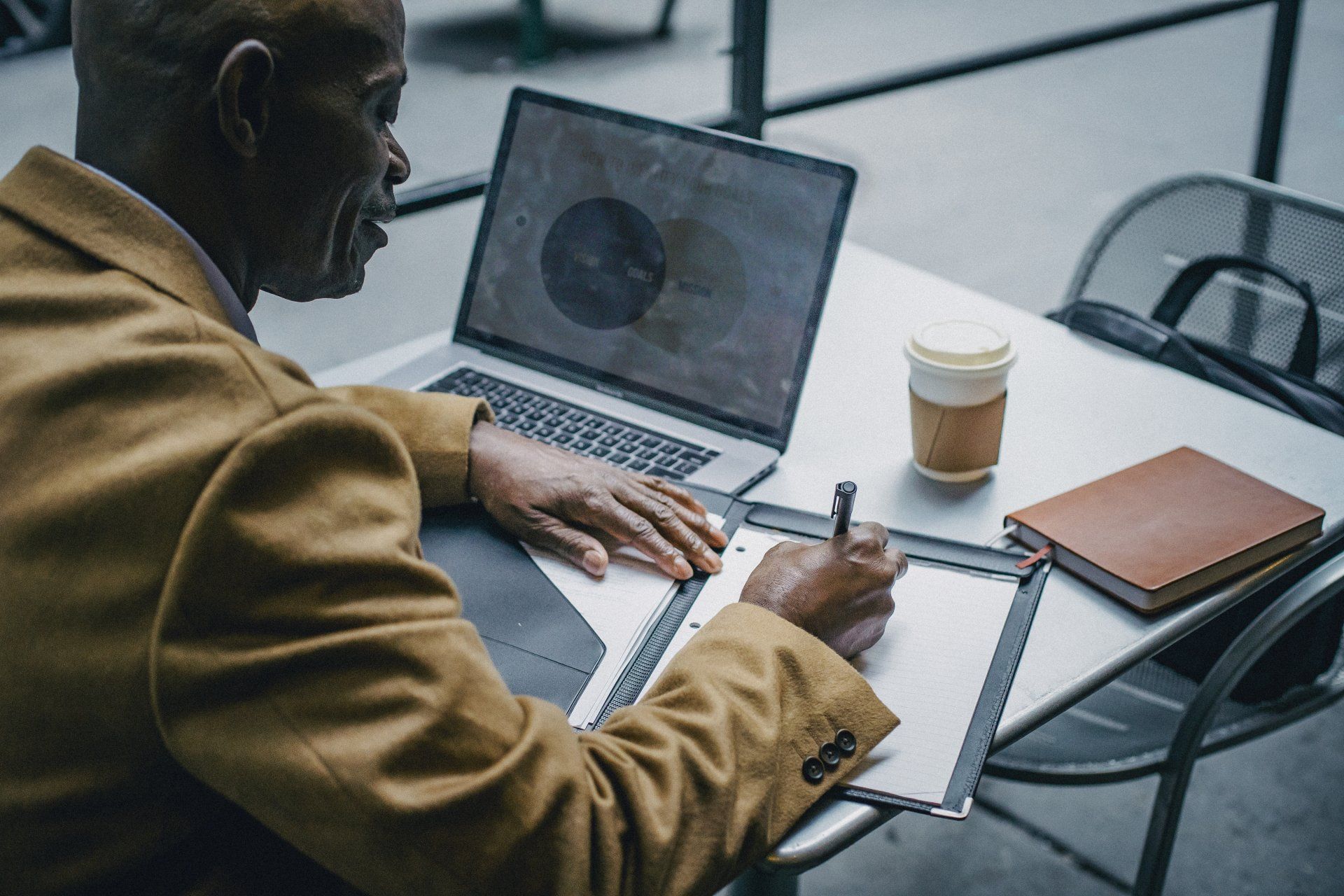 A man is sitting at a table with a laptop and a cup of coffee.