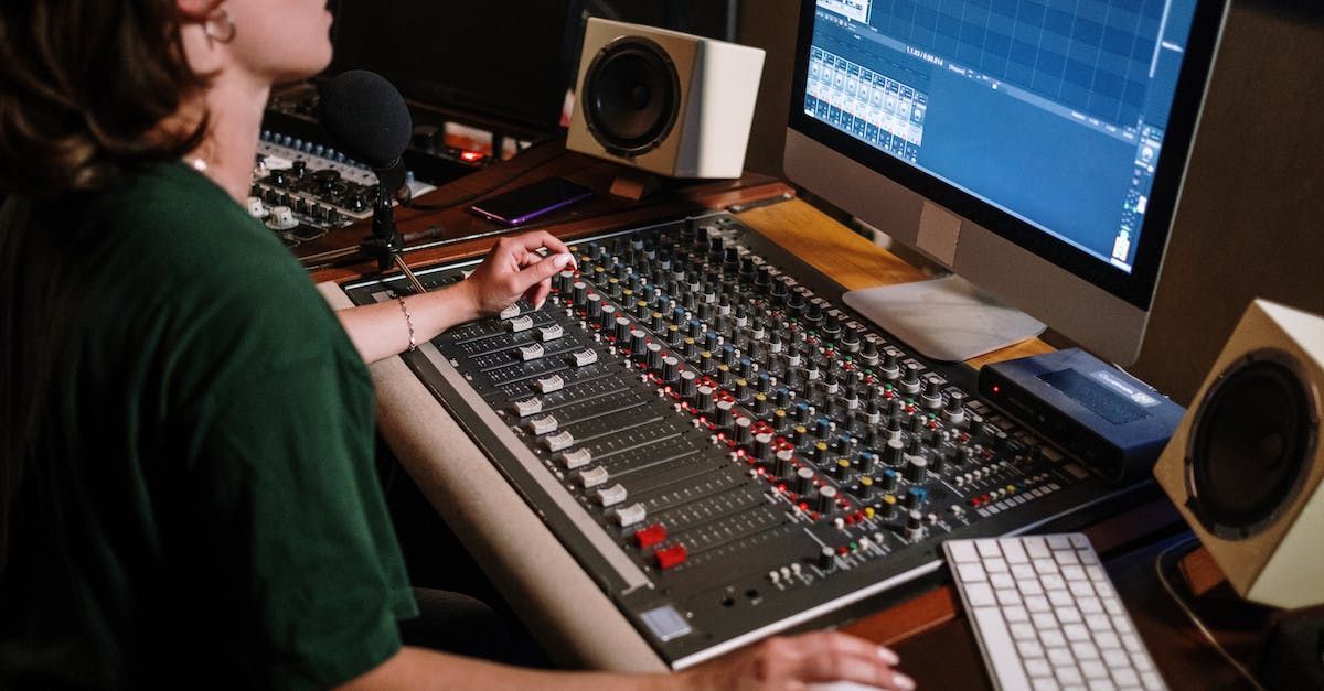 A man is sitting at a desk in front of a computer and a mixer.