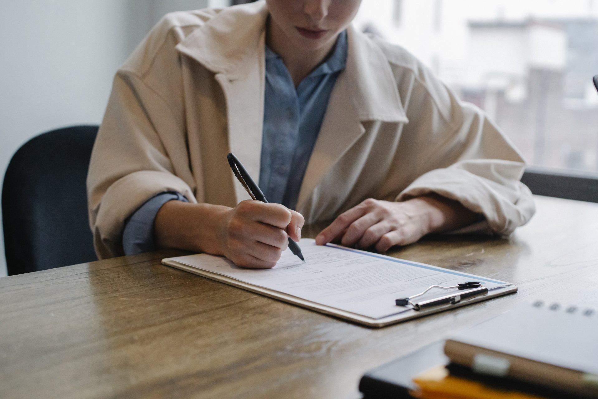 A woman is sitting at a table writing on a clipboard.