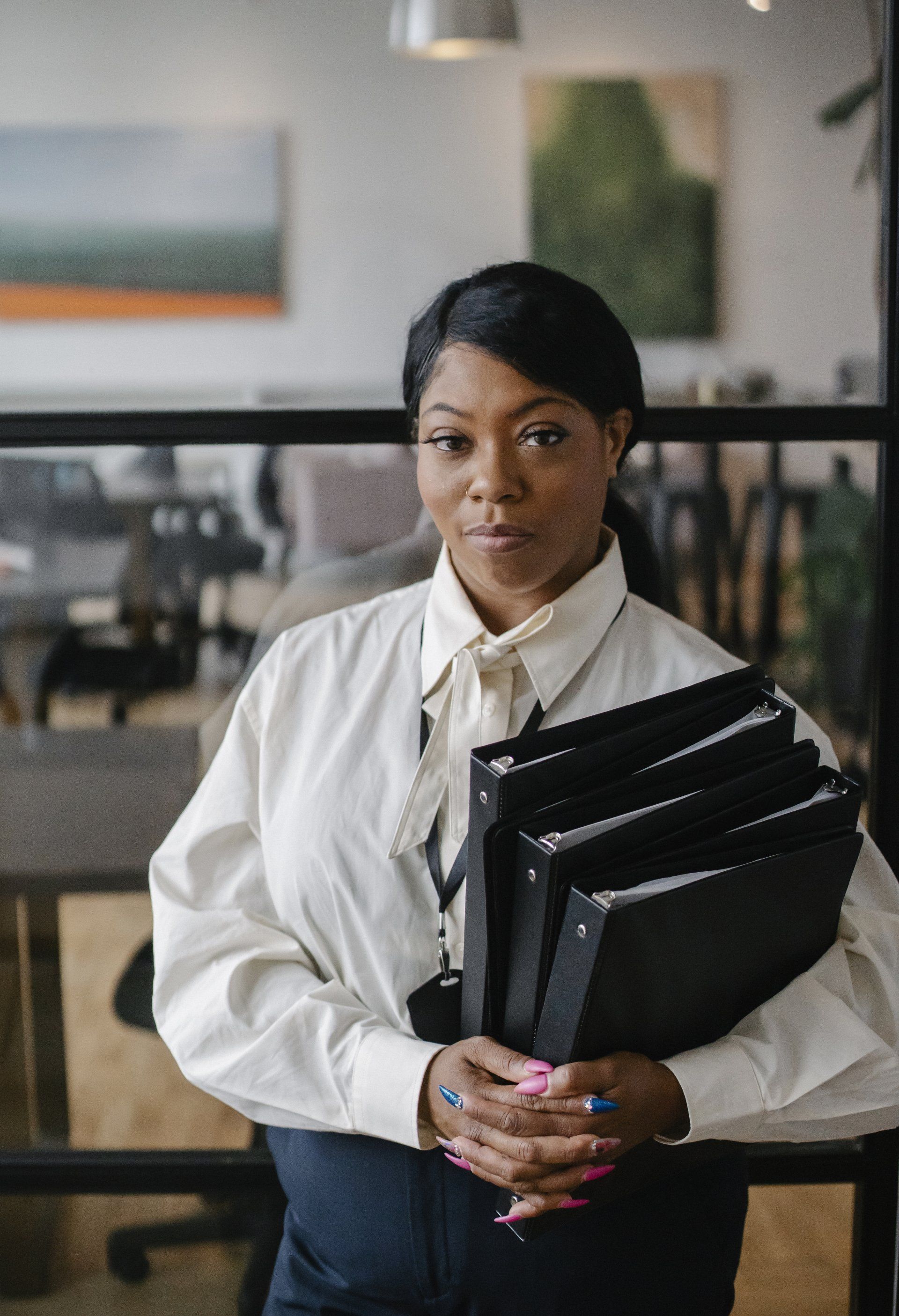 A woman in a white shirt and tie is holding a stack of folders.