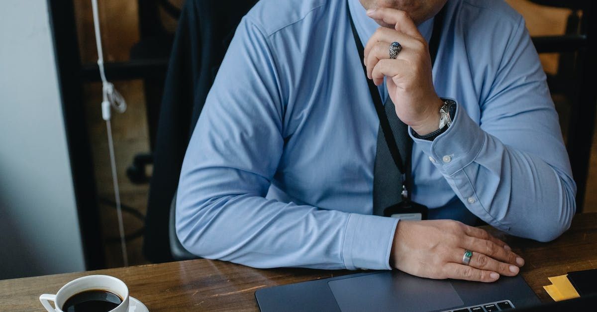A man in a blue shirt and tie is sitting at a table with a cup of coffee.