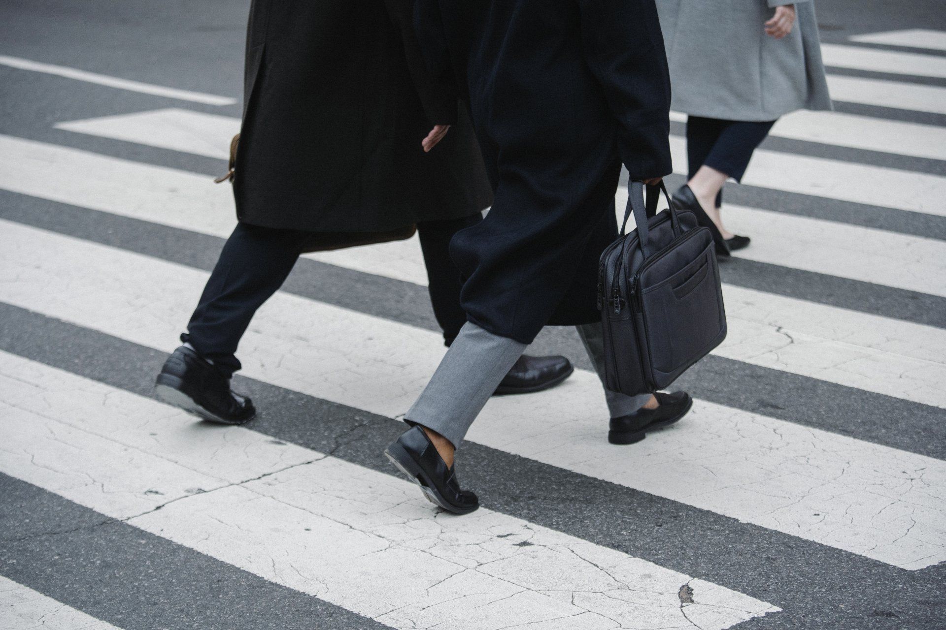 People walking across a crosswalk. One person carries a briefcase; they wear dark coats and pants.