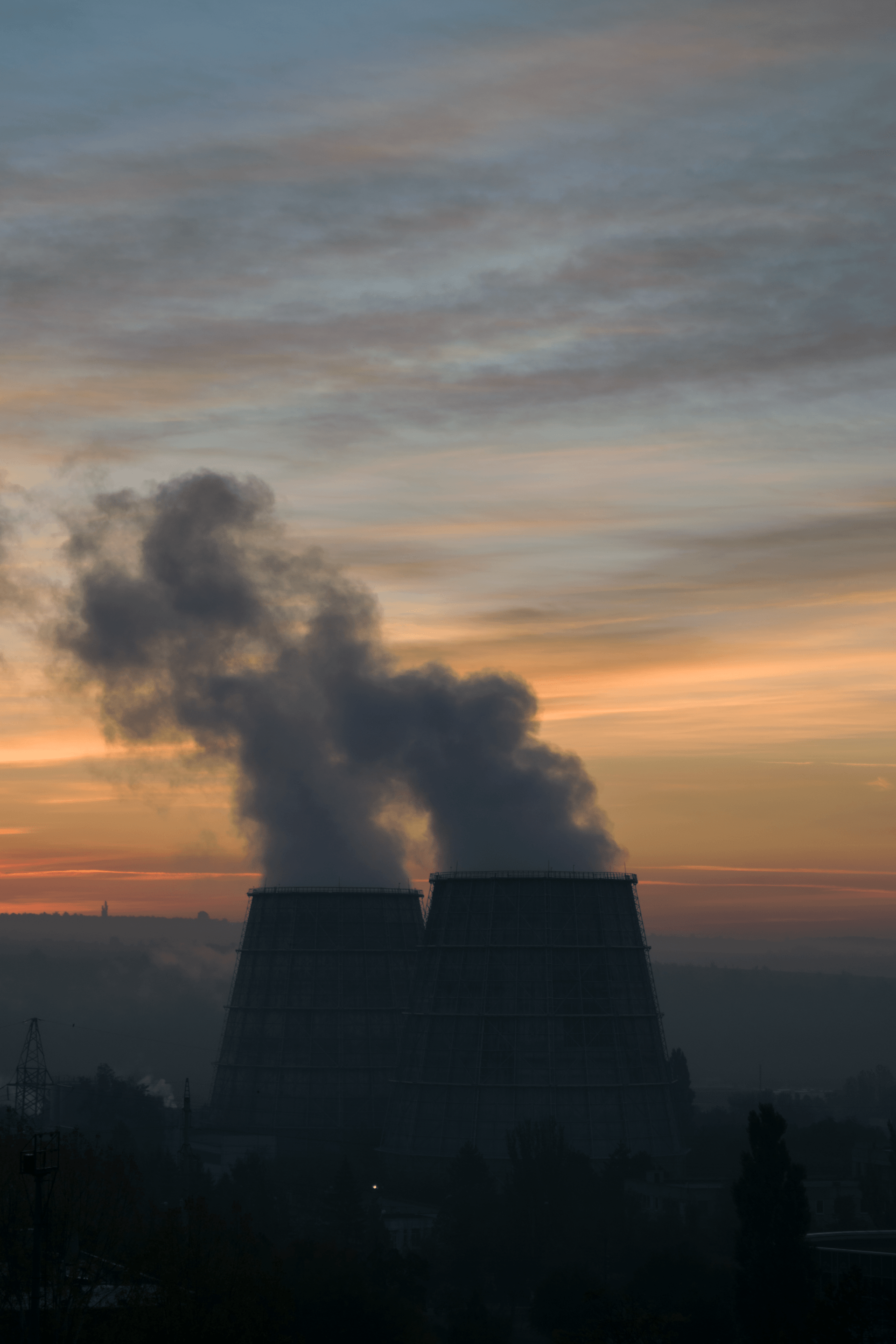 Two industrial smokestacks emitting smoke against a colorful sunrise sky.