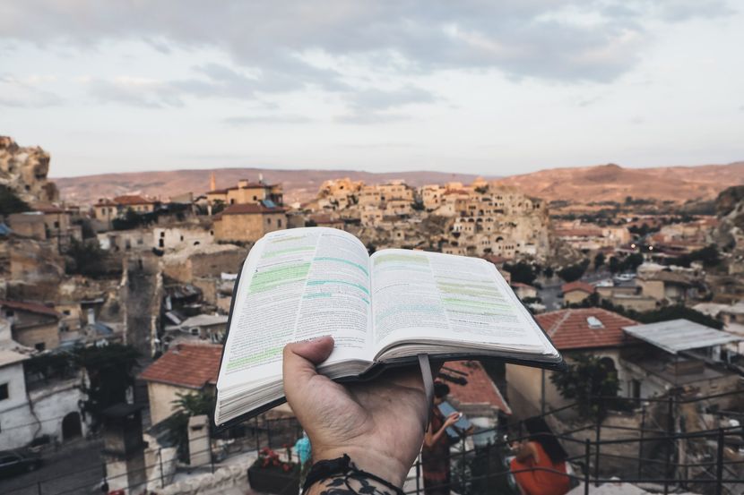 A person is holding an open book in front of a city.