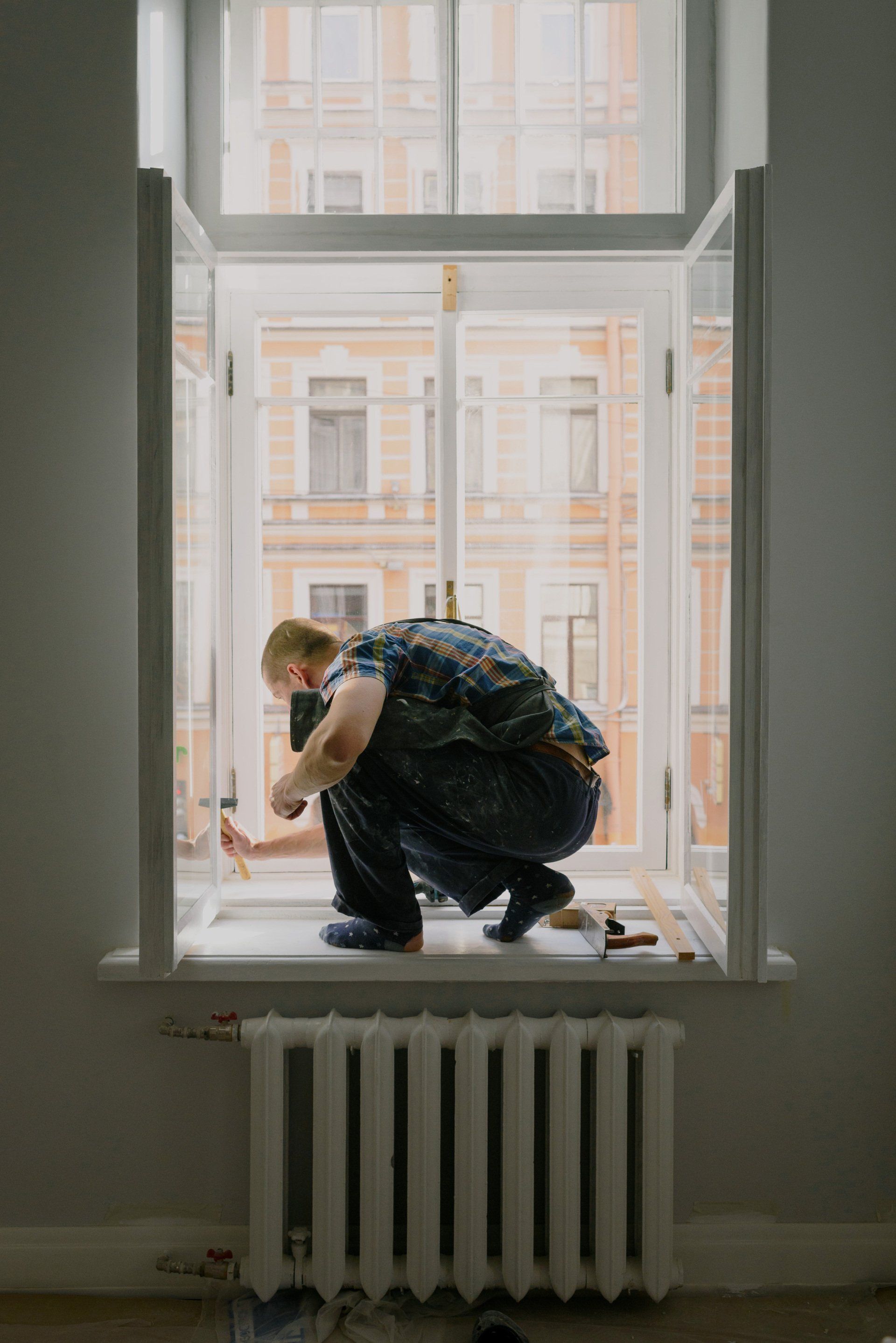A man is kneeling on a window sill working on a window.