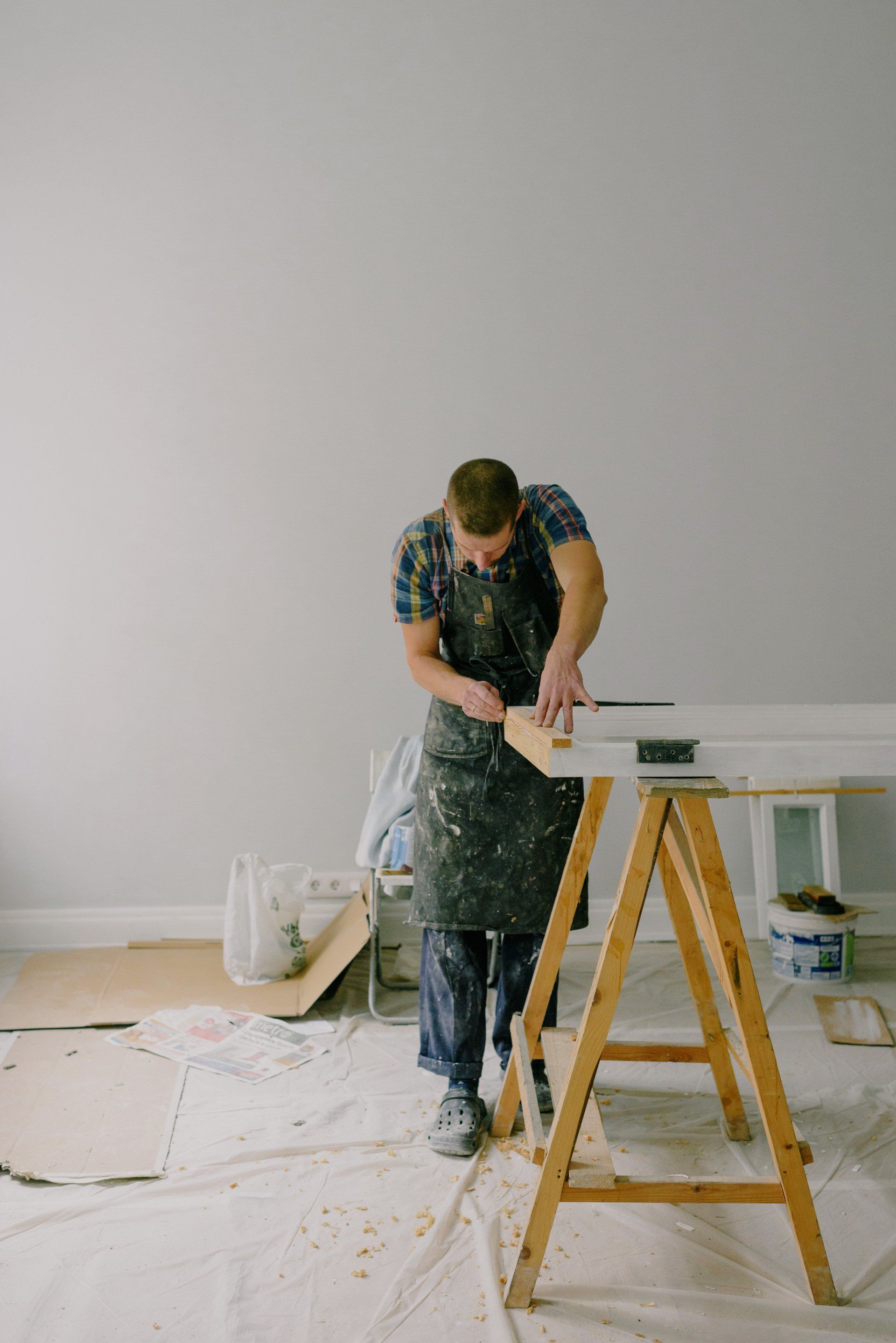 Man in apron sawing wood on a worktable in a room under renovation.