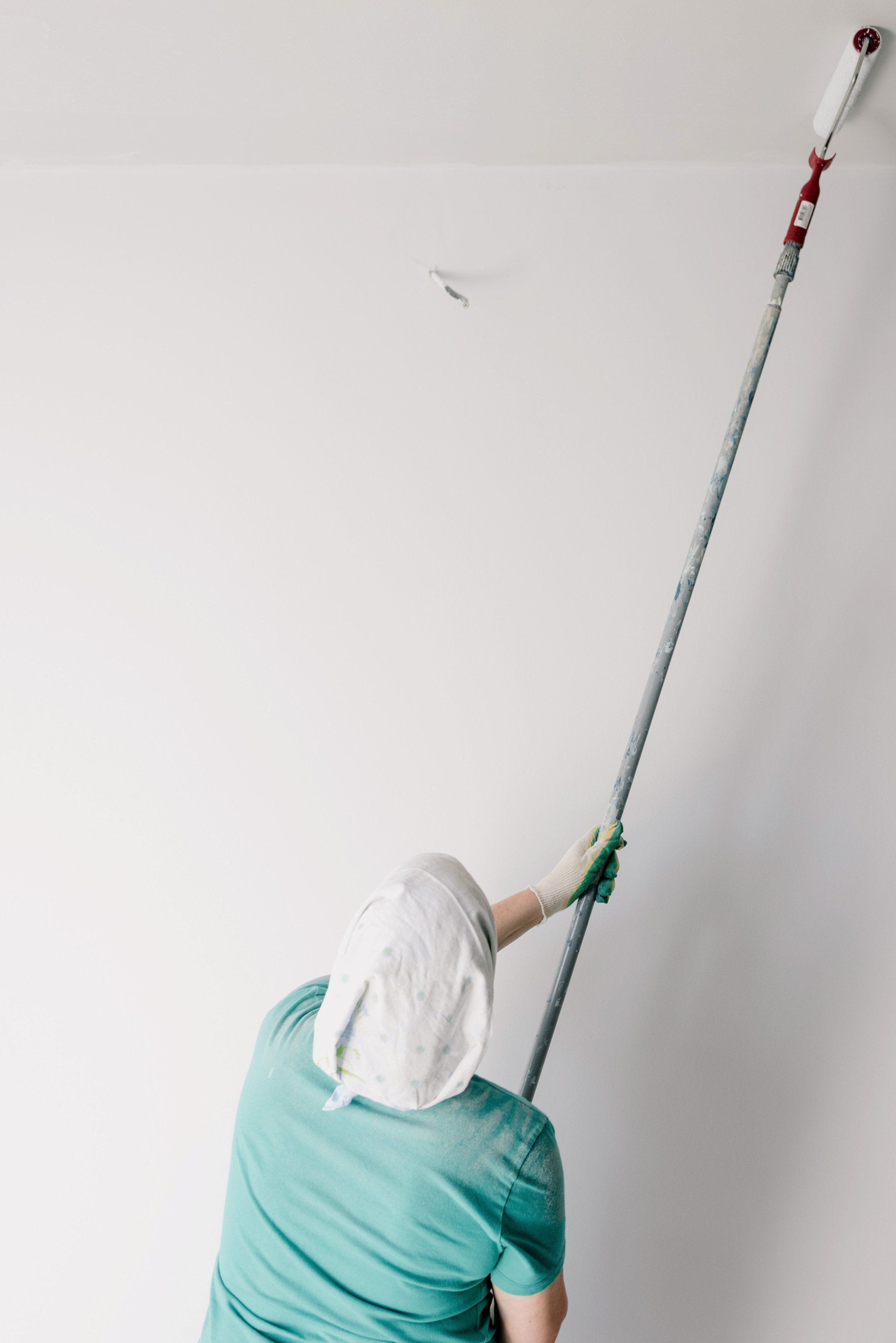 Person painting a ceiling with a long-handled roller in a white room