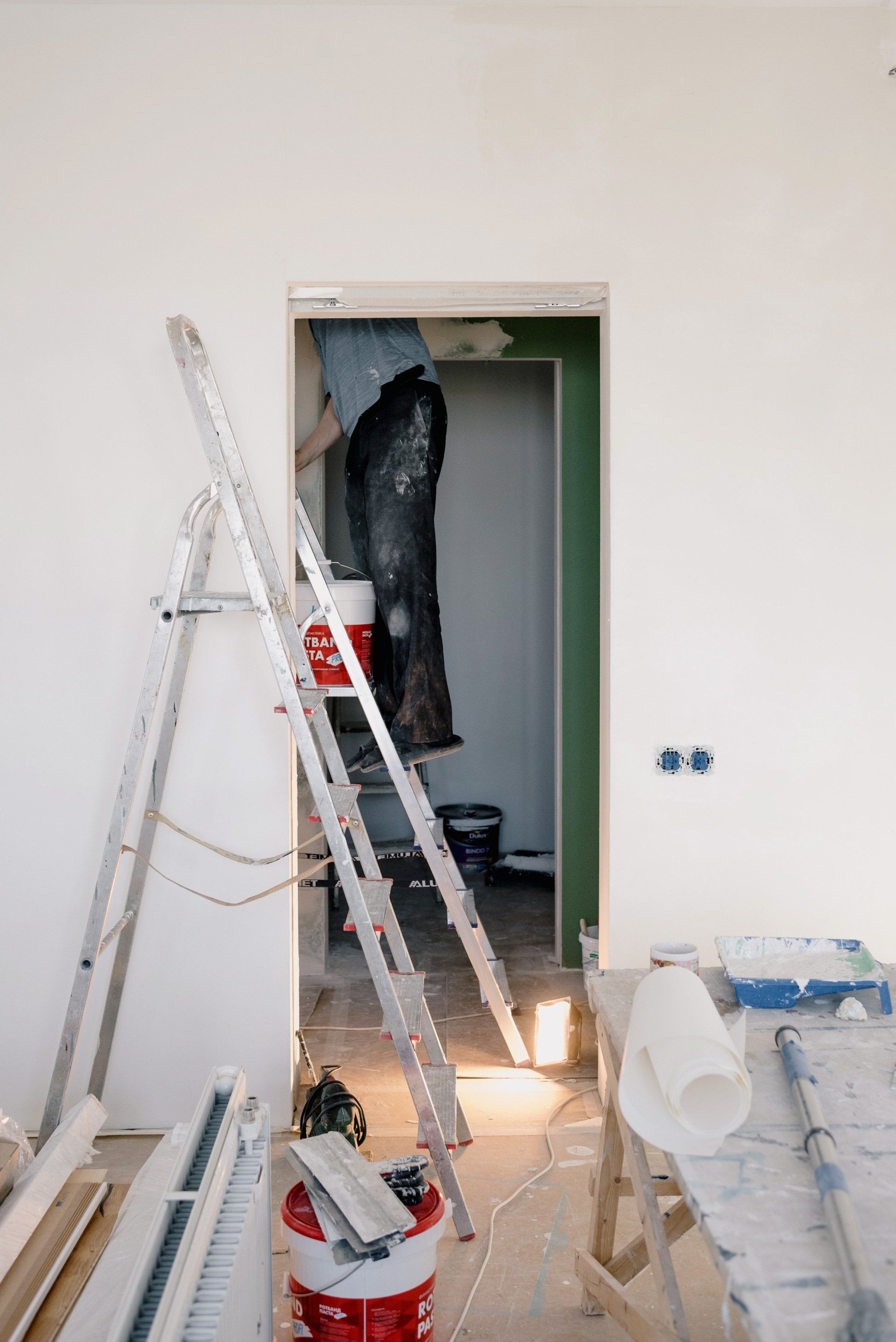 A man is standing on a ladder in a room under construction.